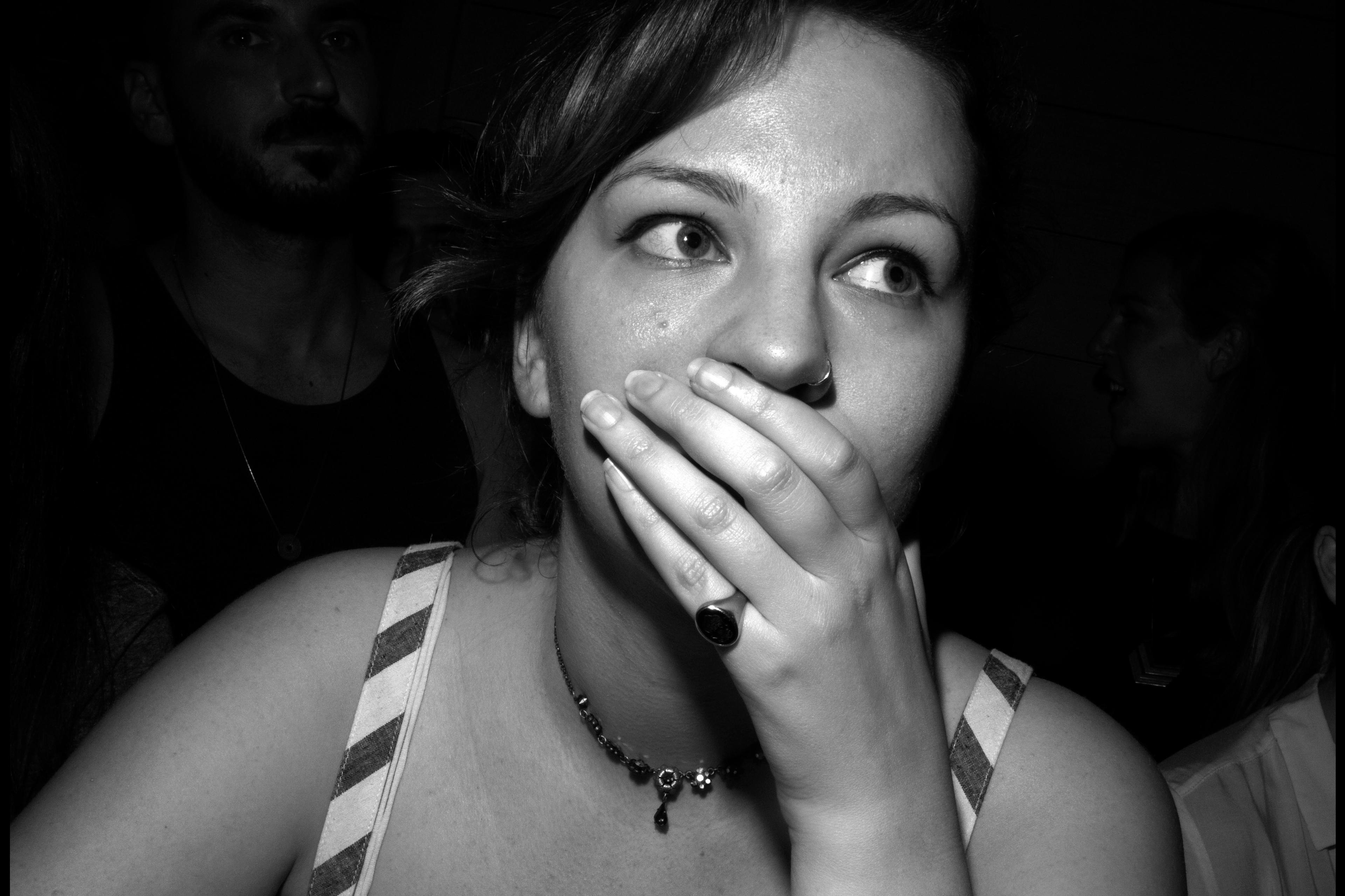 Black and white photo of a woman covering her mouth with her hand in a crowded room.