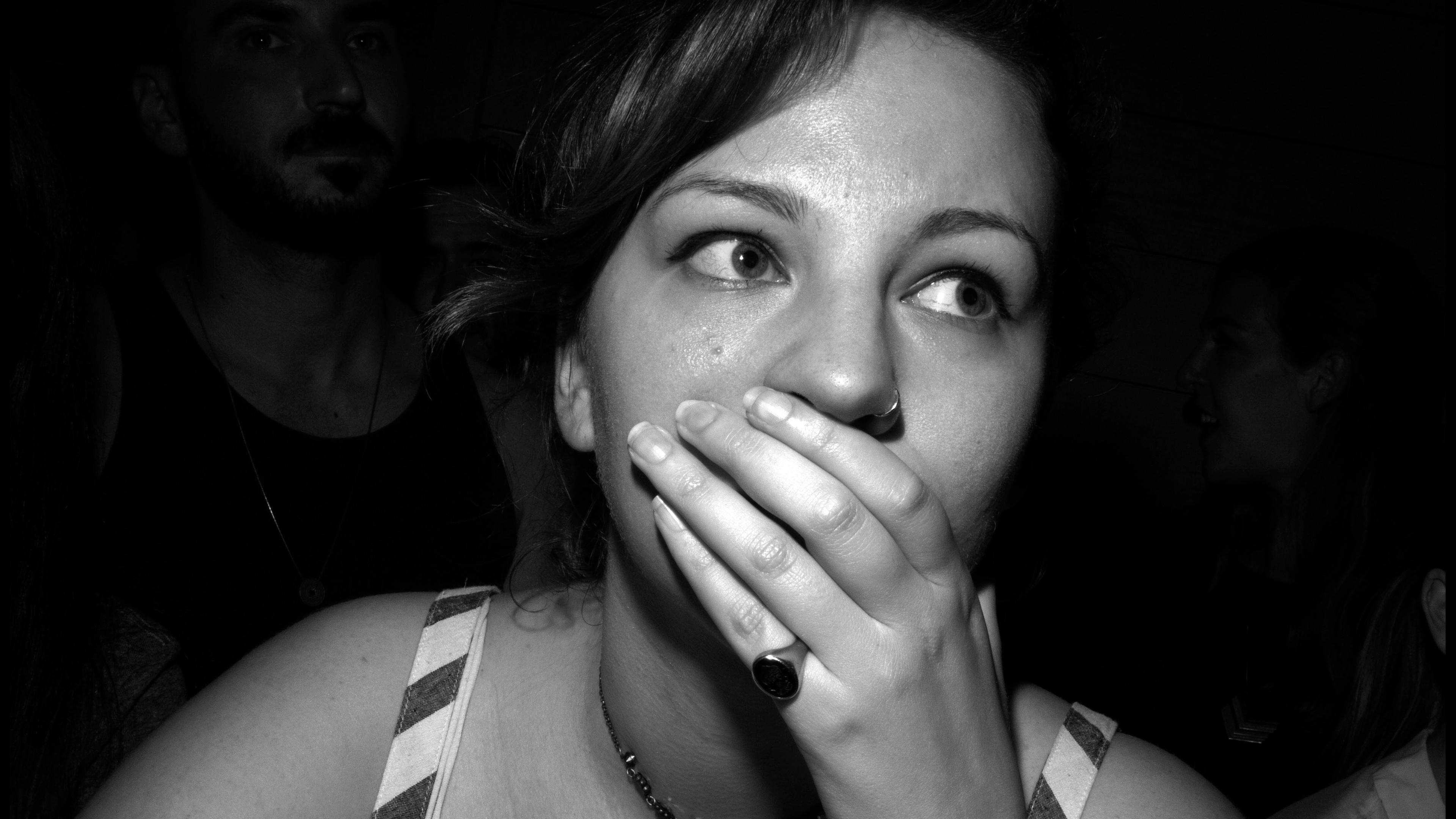 Black and white photo of a woman covering her mouth with her hand in a crowded room.