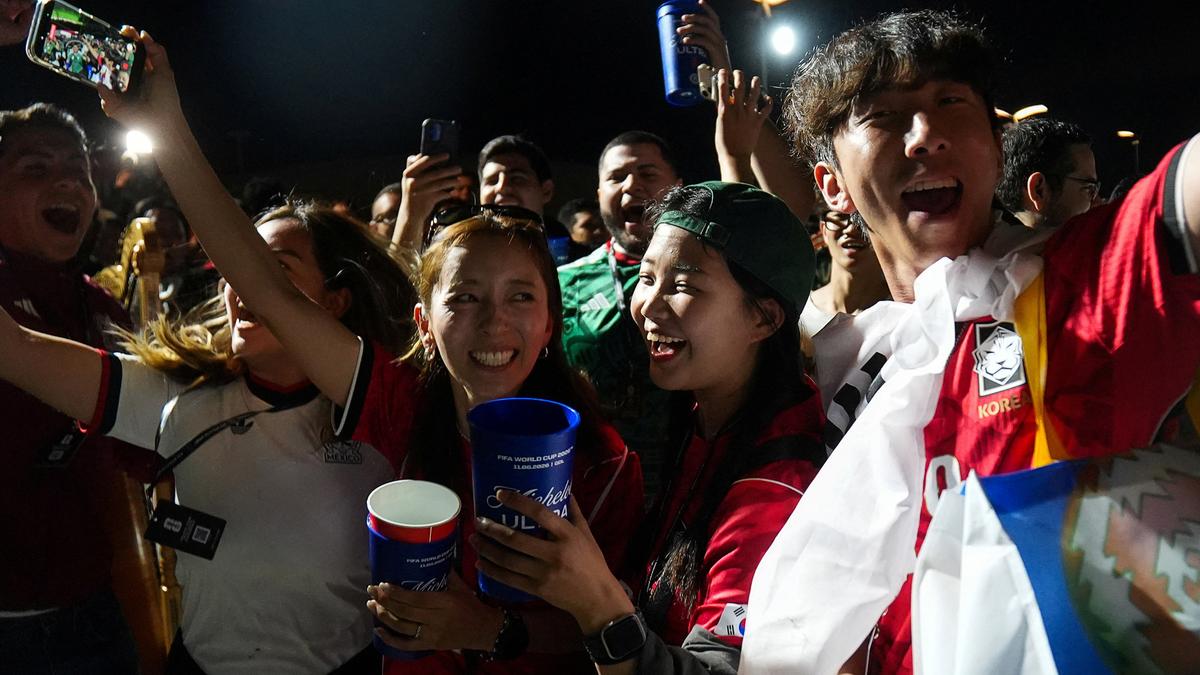 Excited football fans in team jerseys celebrating, some holding cups, others taking selfies at night.