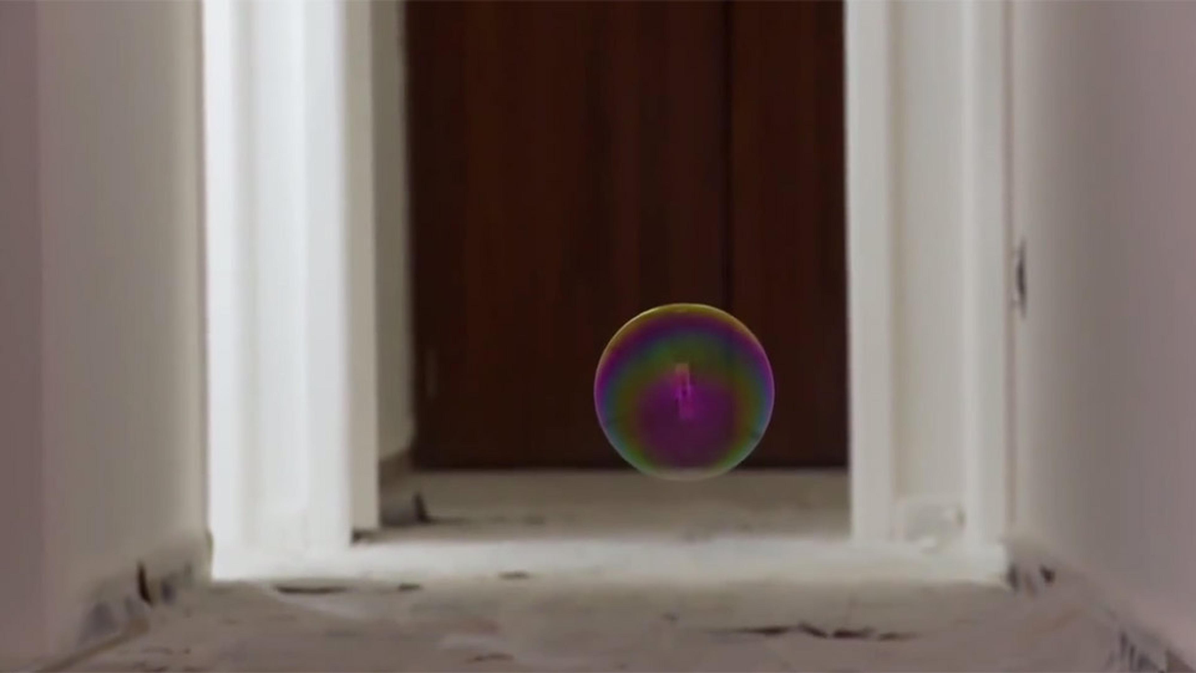 A colourful soap bubble floating in the middle of a white-painted hallway with a wooden door at the end.