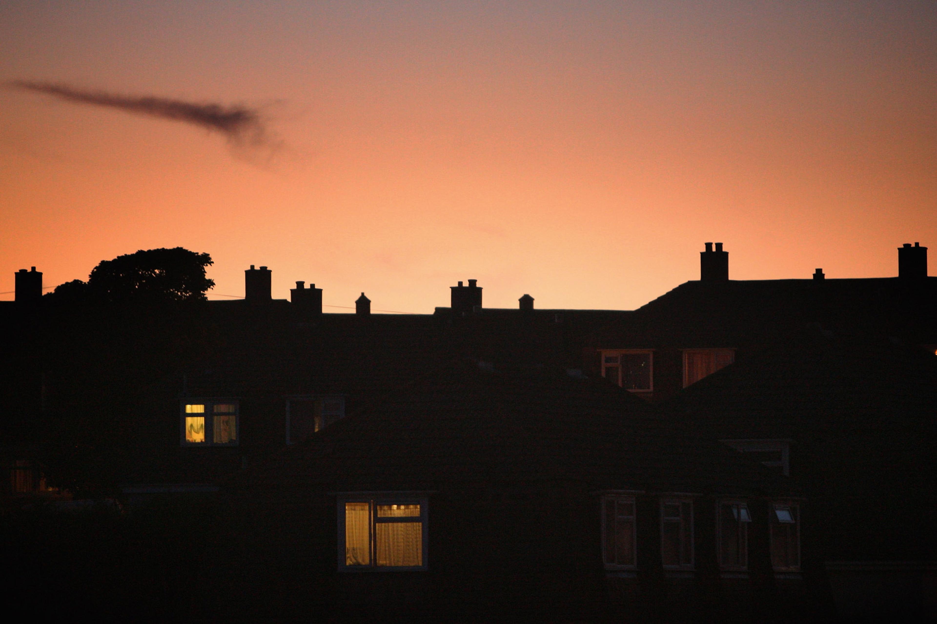 Photo of silhouetted rooftops at sunset with lit windows and an orange sky.