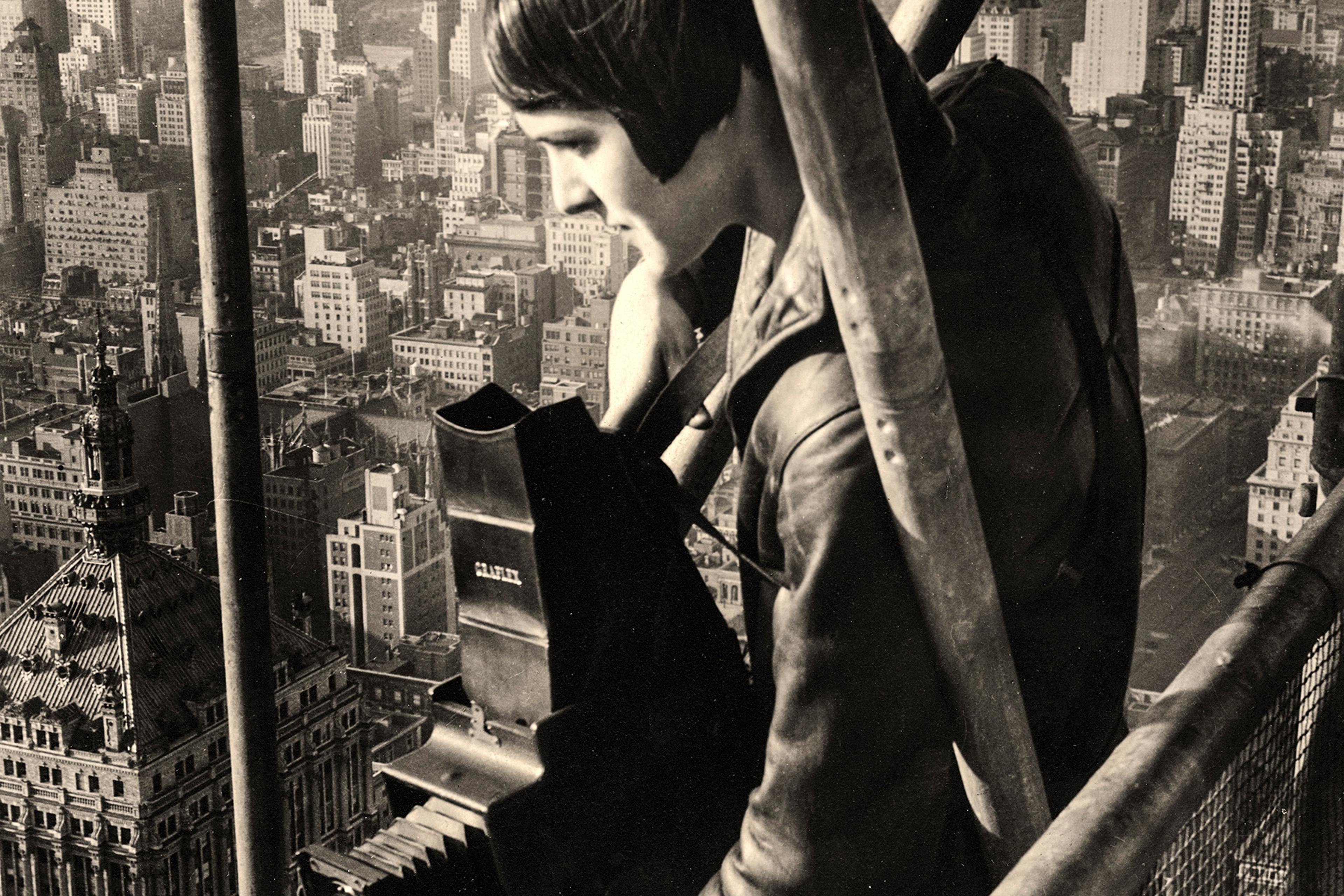 Vintage photo of a woman with a box camera on a high scaffold overlooking a large cityscape.