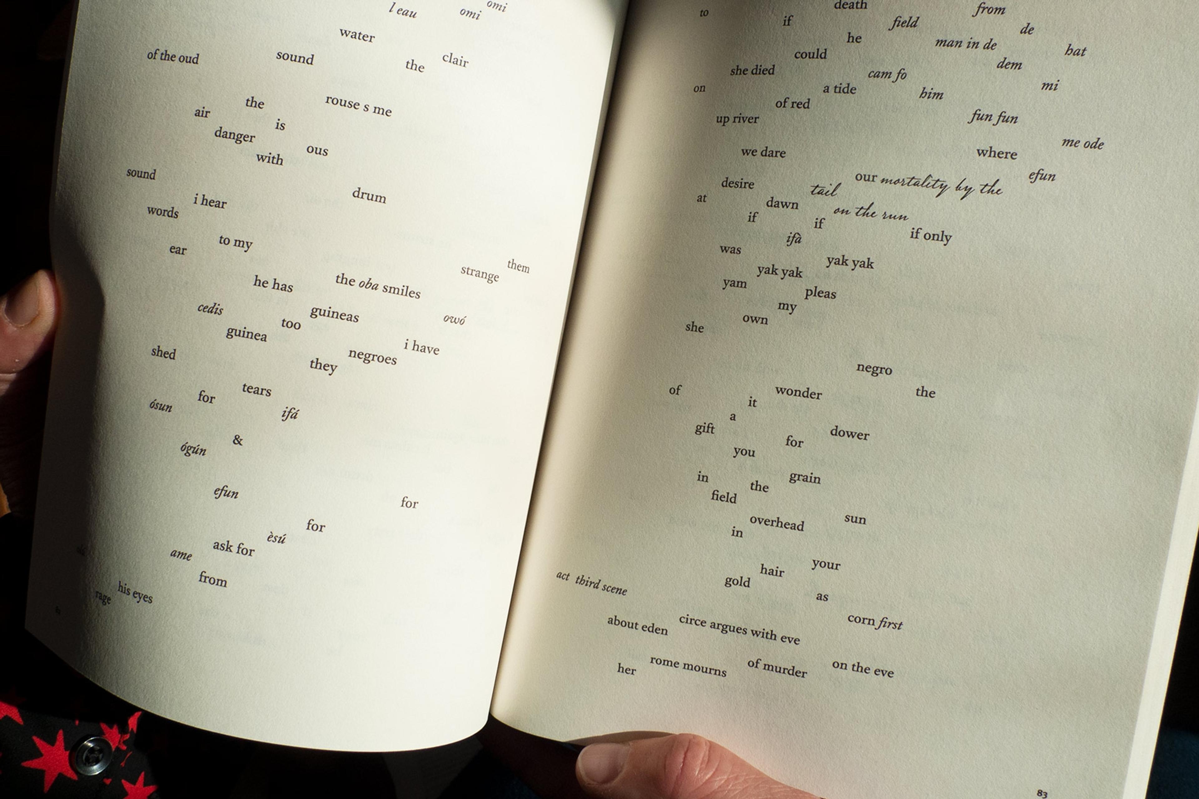 Photo of an open book with scattered text, held by hands. The text appears as a poetic or artistic composition.
