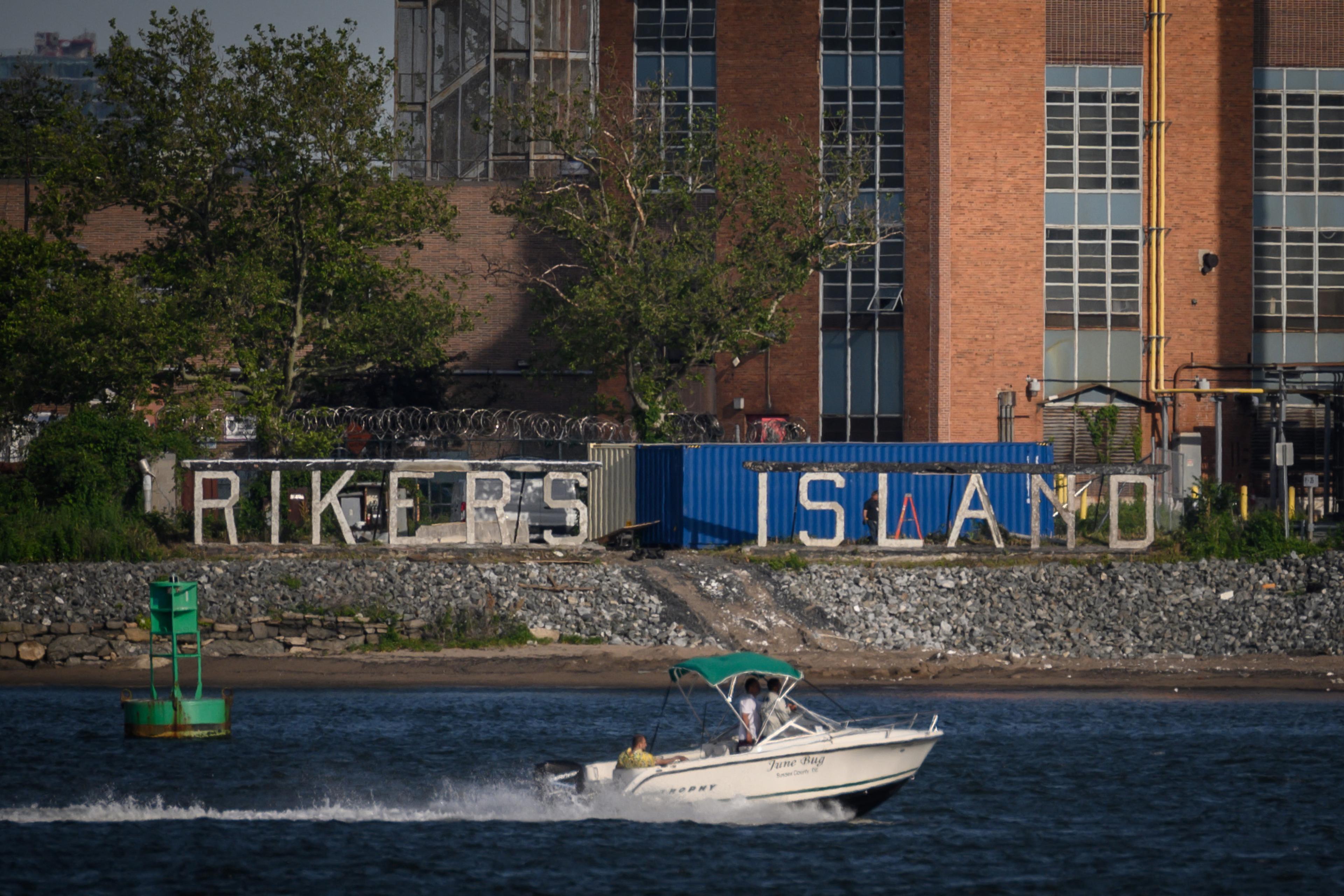 Rikers Island sign on a building with a speedboat on the river in the foreground.