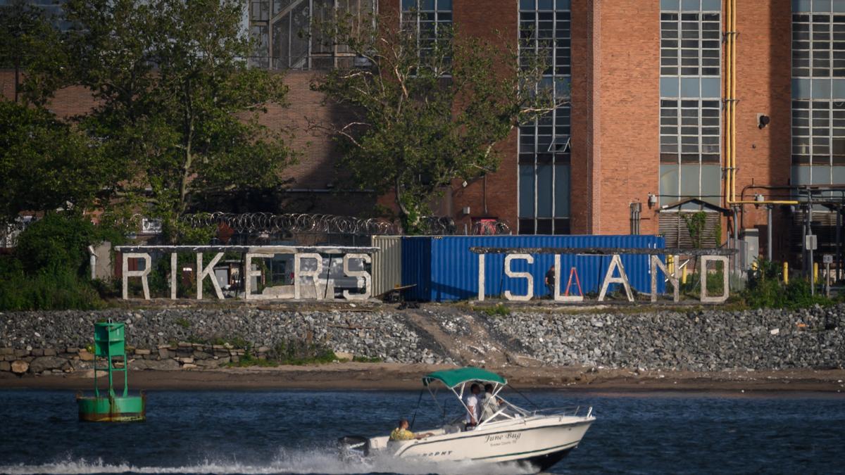 Rikers Island sign on a building with a speedboat on the river in the foreground.