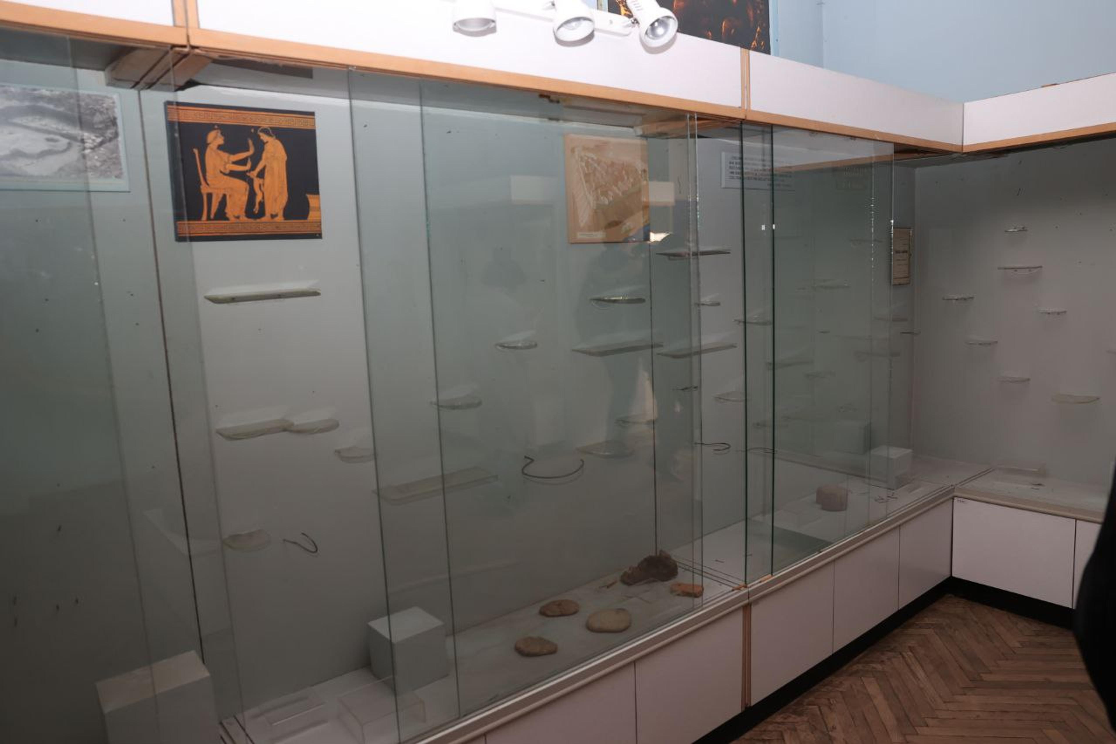 An empty glass display case in a museum with a painting of two figures and some rocks at the bottom.