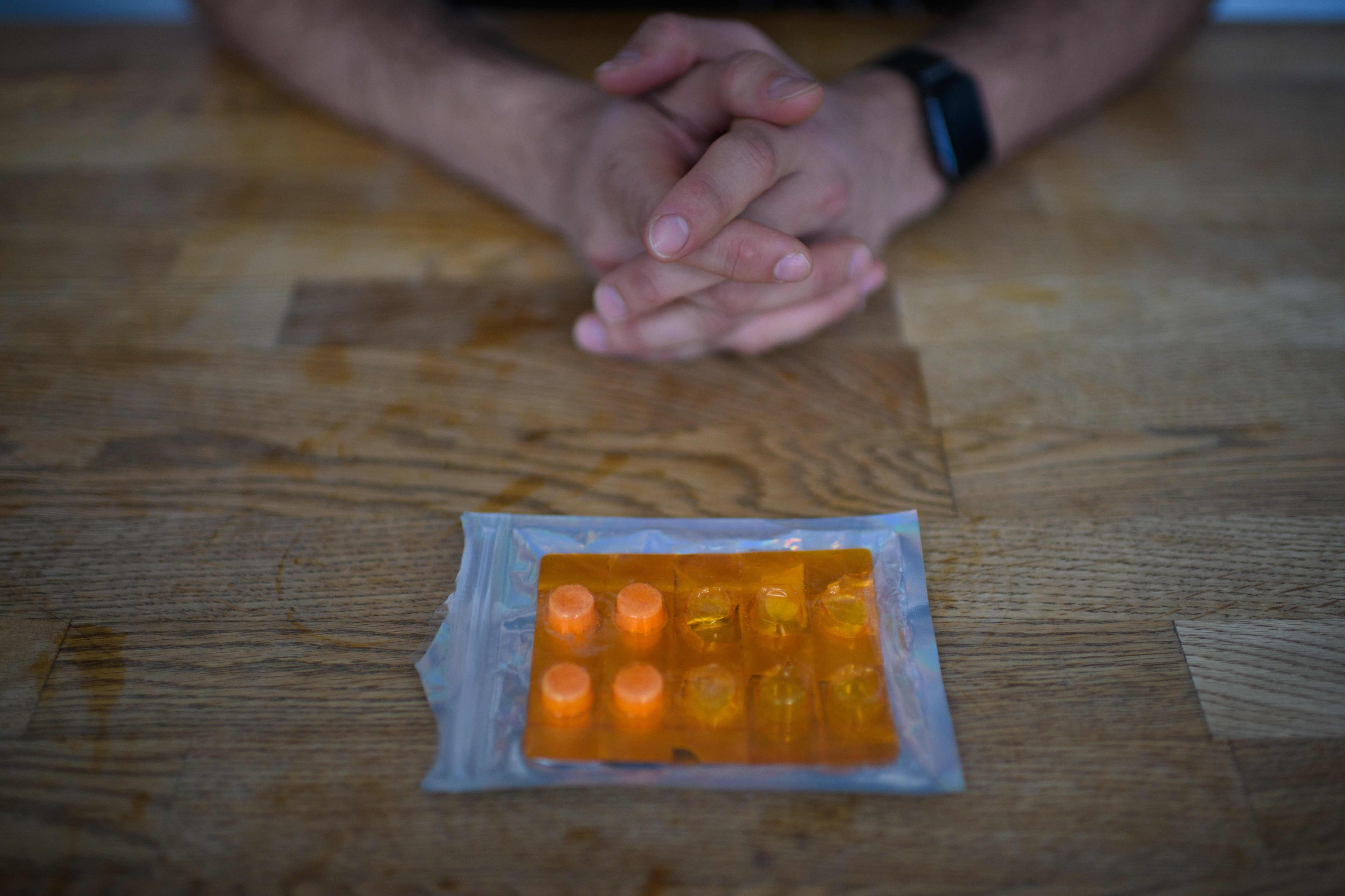 Photo of hands clasped on a wooden table with a blister pack of orange pills in front.