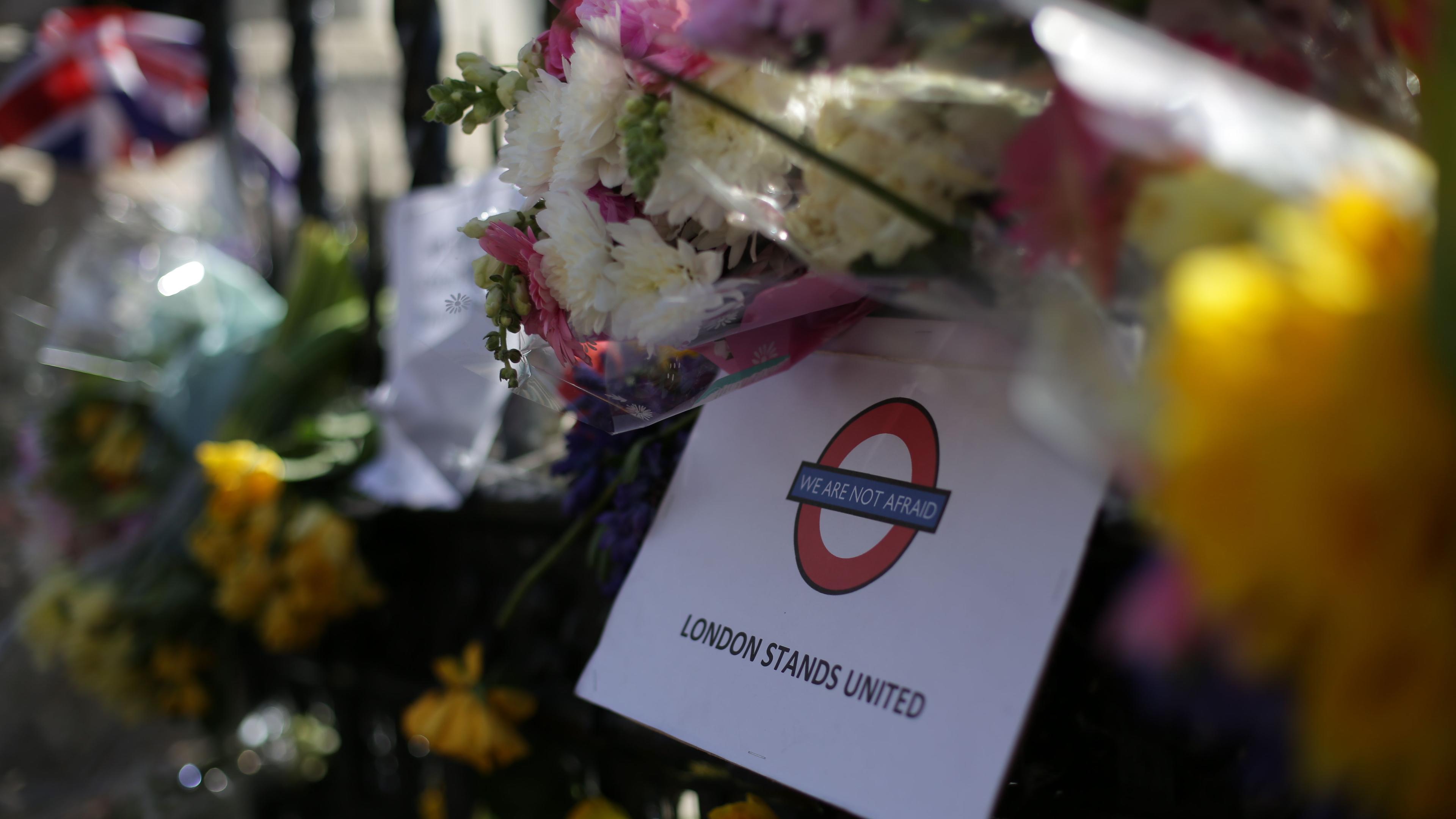 Photo of flowers with a sign reading “London Stands United” and “We Are Not Afraid” in London Underground style.