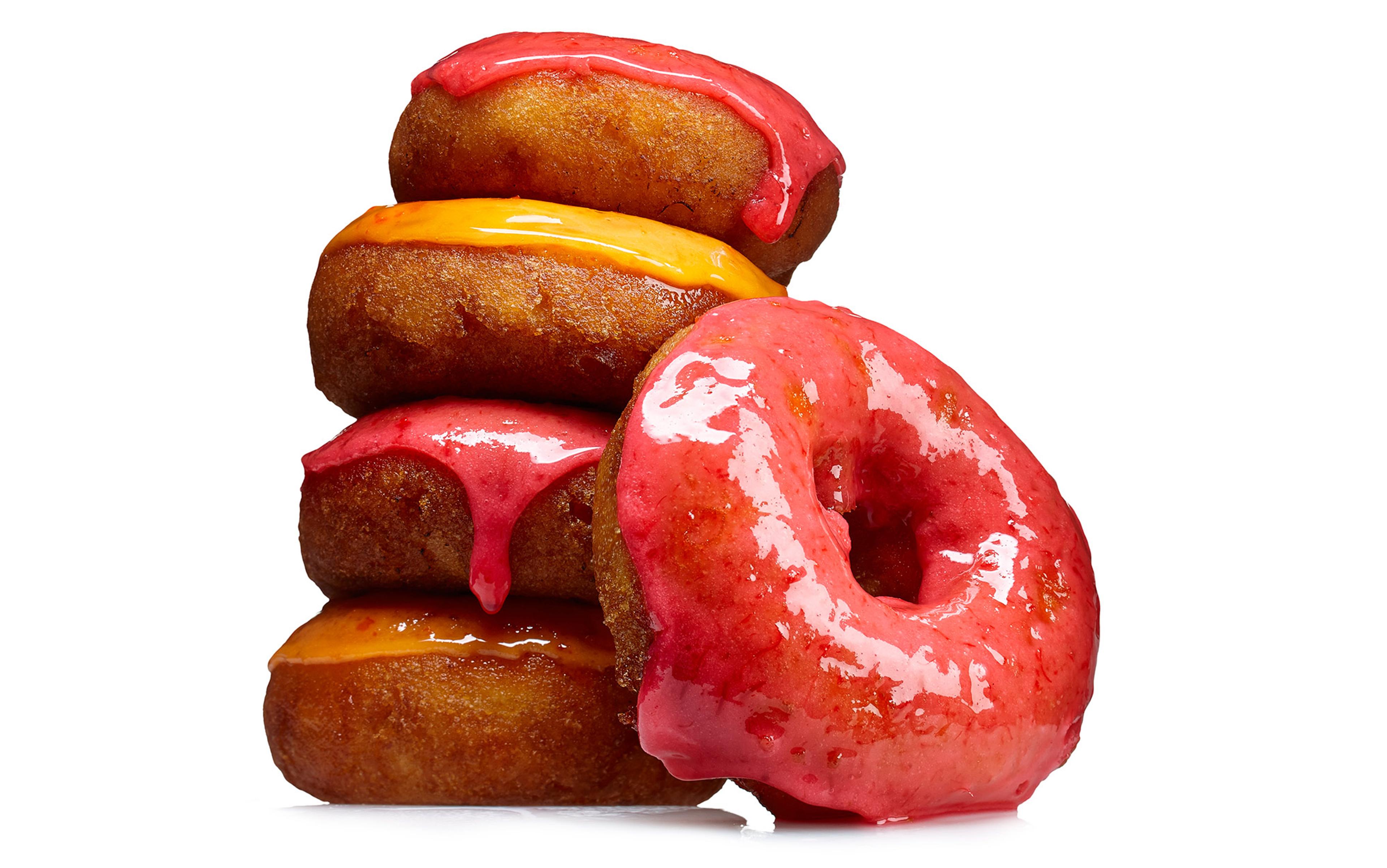 Four stacked doughnuts with red and orange icing, with one doughnut leaning against the stack, all on a white background.