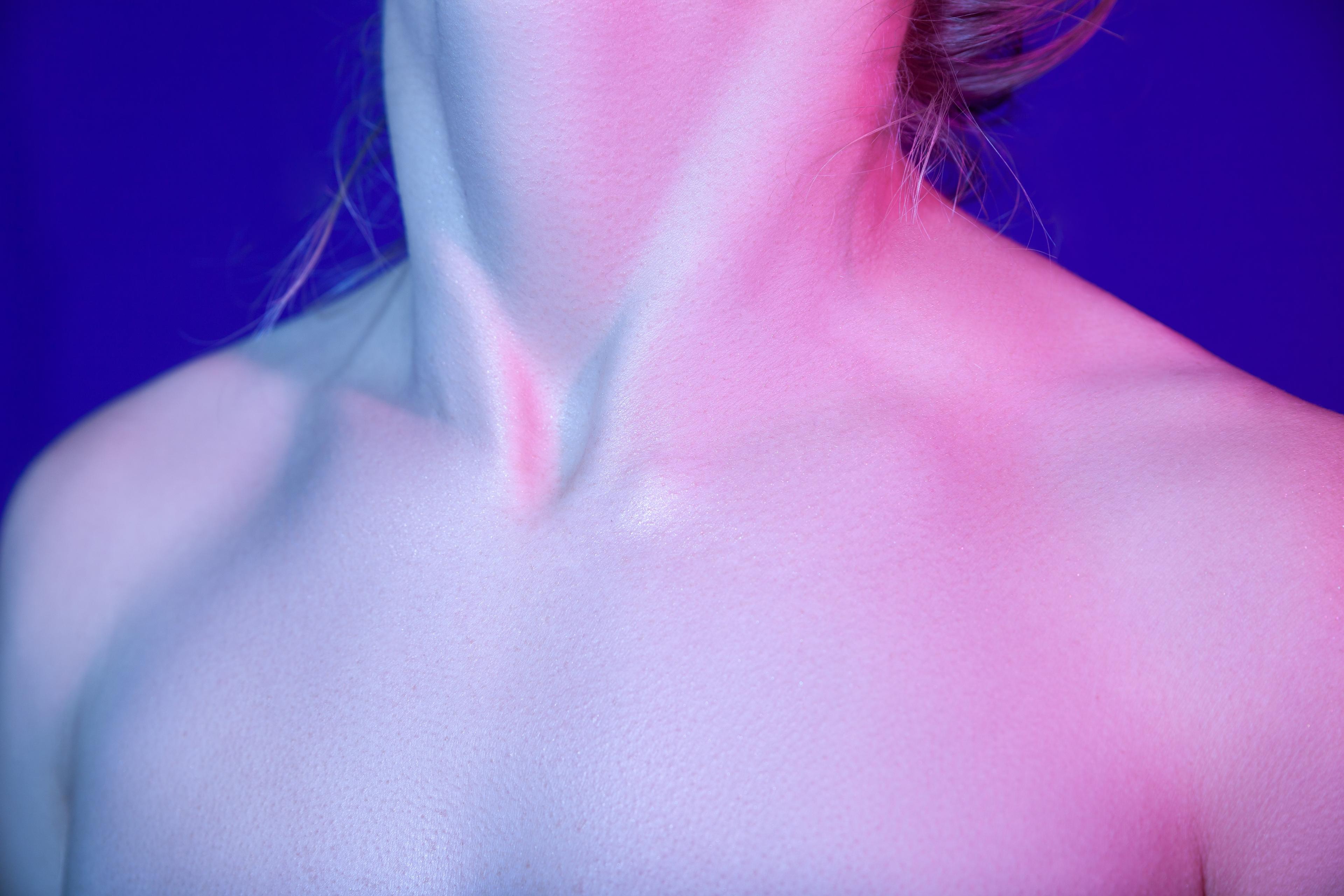 Photo of a person’s neck and shoulders illuminated with pink and blue light on a dark blue background.