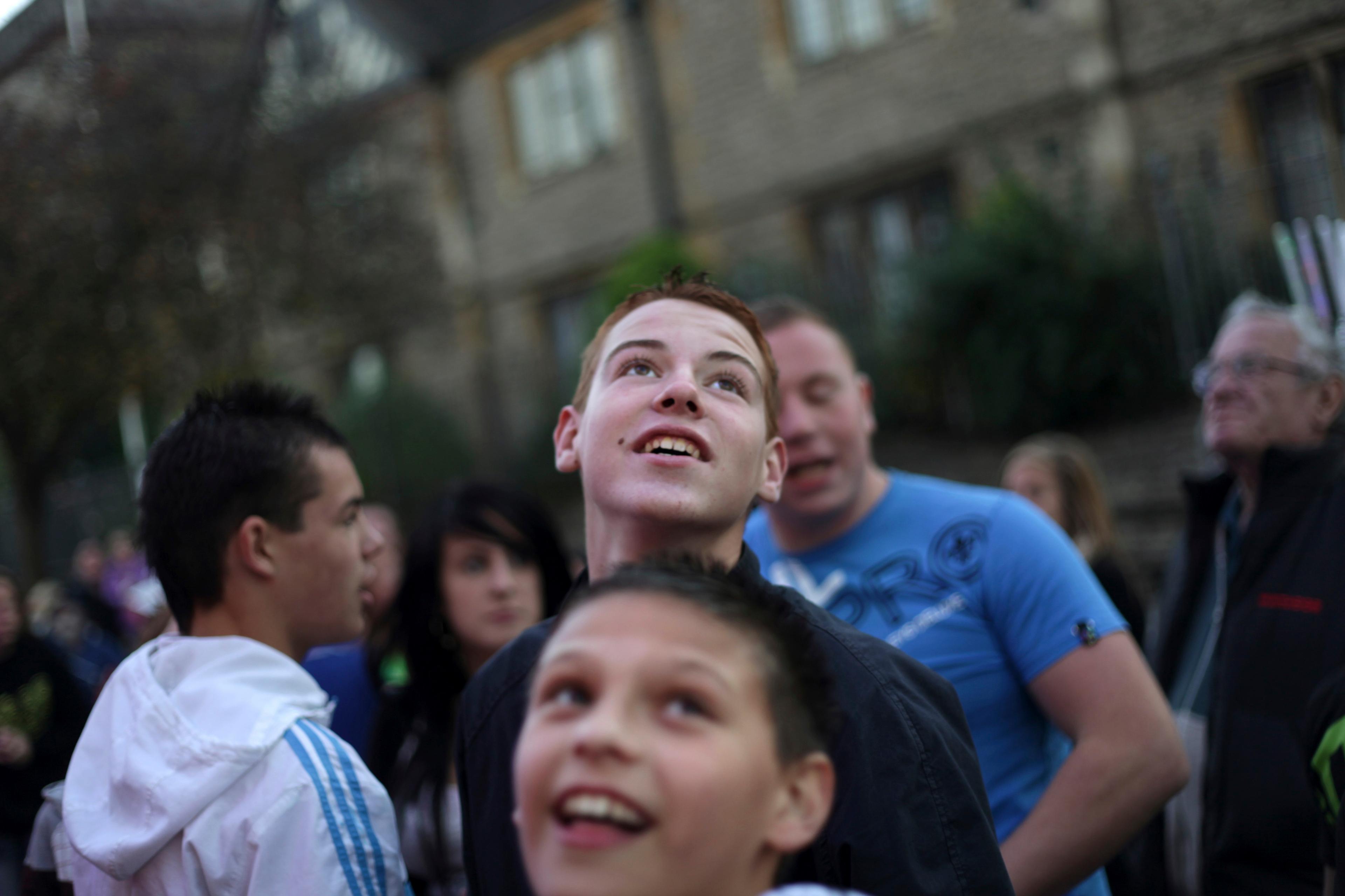 Photo of a group of people outdoors looking upwards, focused expressions, blurred background of buildings and trees.