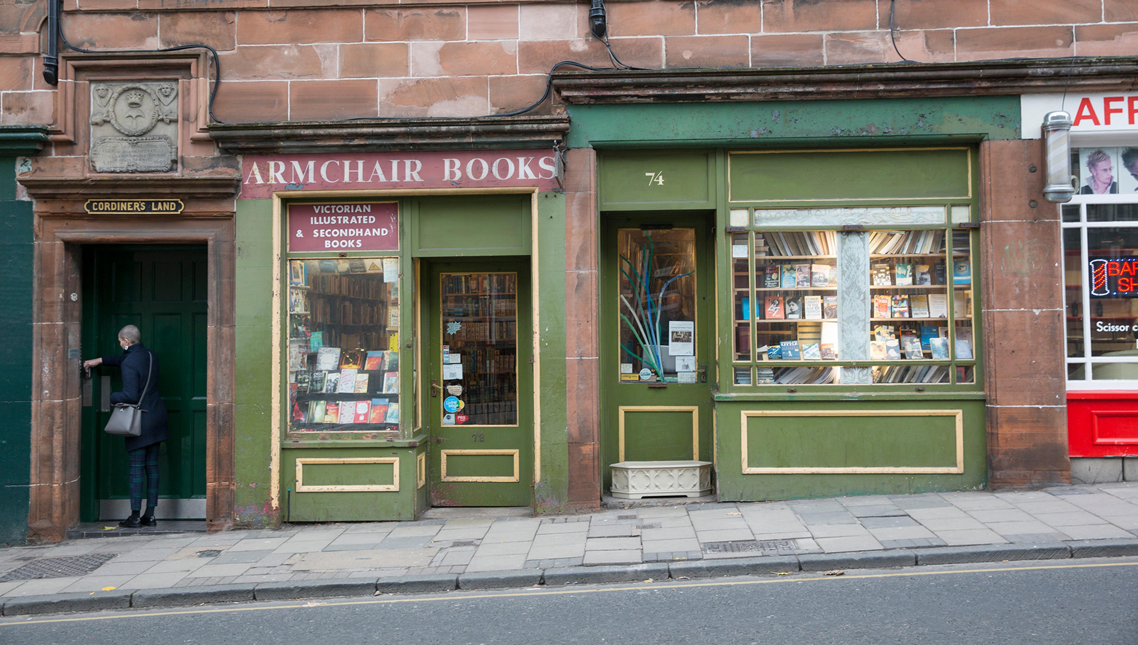 Photo of a street with a person entering a doorway to the left and a bookshop named Armchair Books displaying books in its windows.