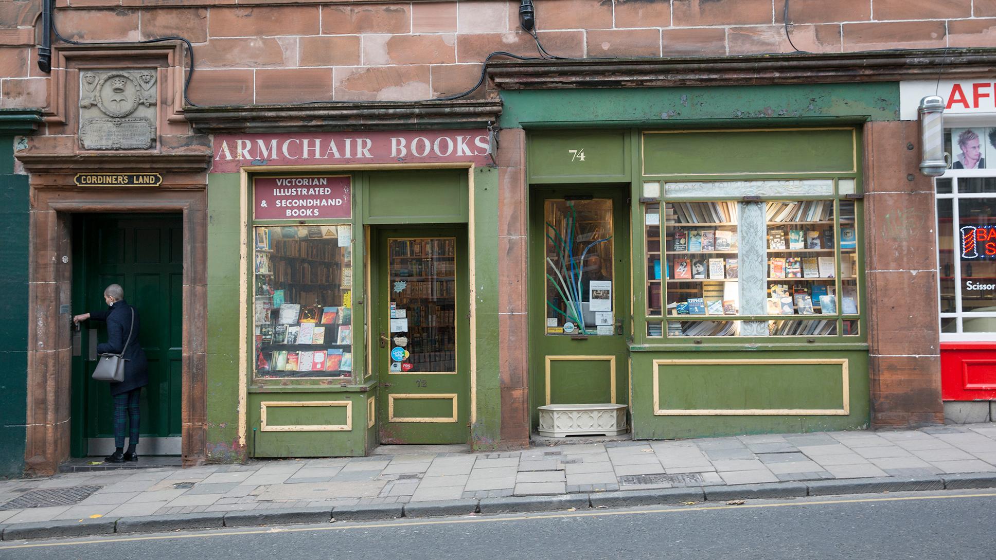 Photo of a street with a person entering a doorway to the left and a bookshop named Armchair Books displaying books in its windows.