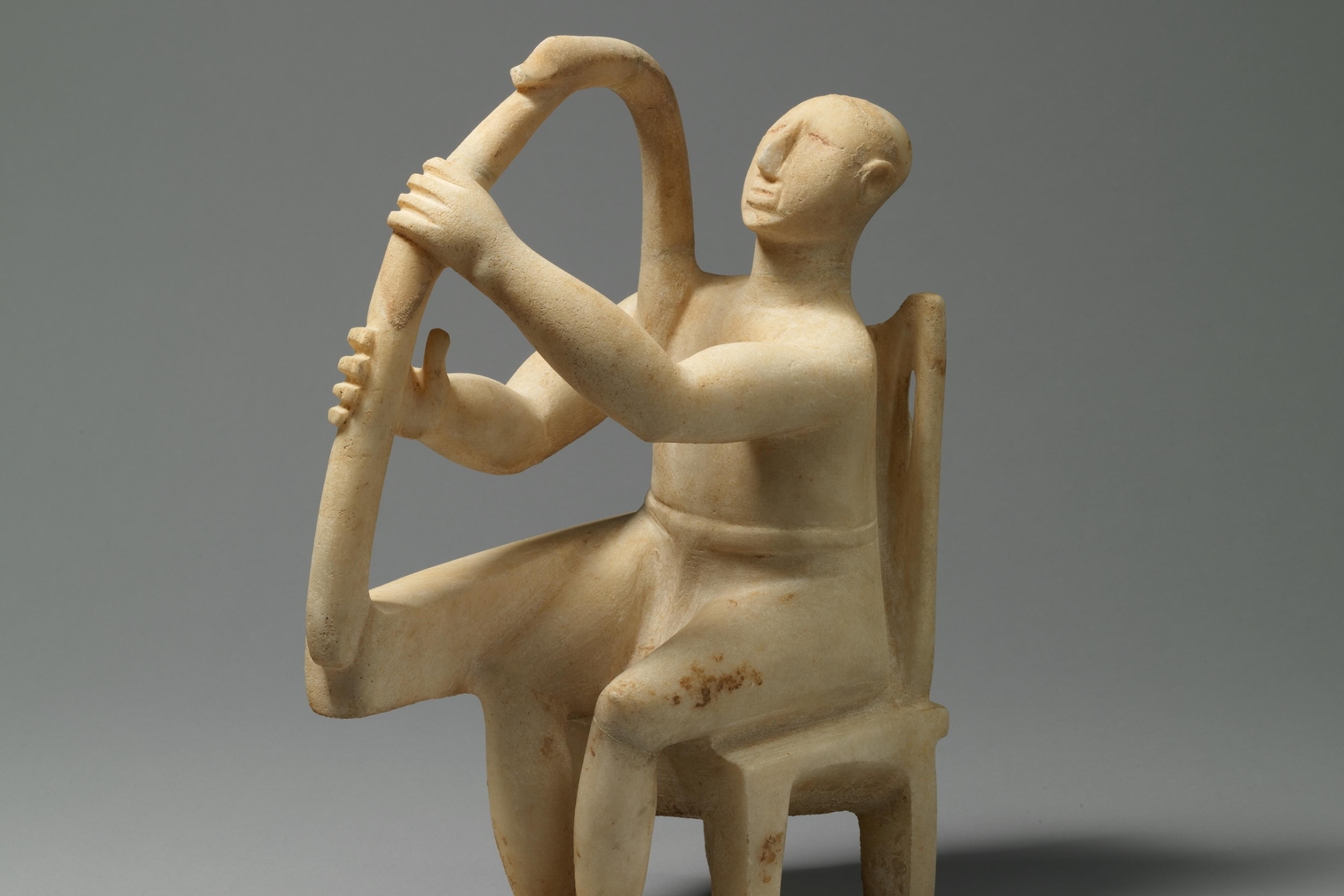 Marble sculpture of a seated figure playing a harp on a grey background.