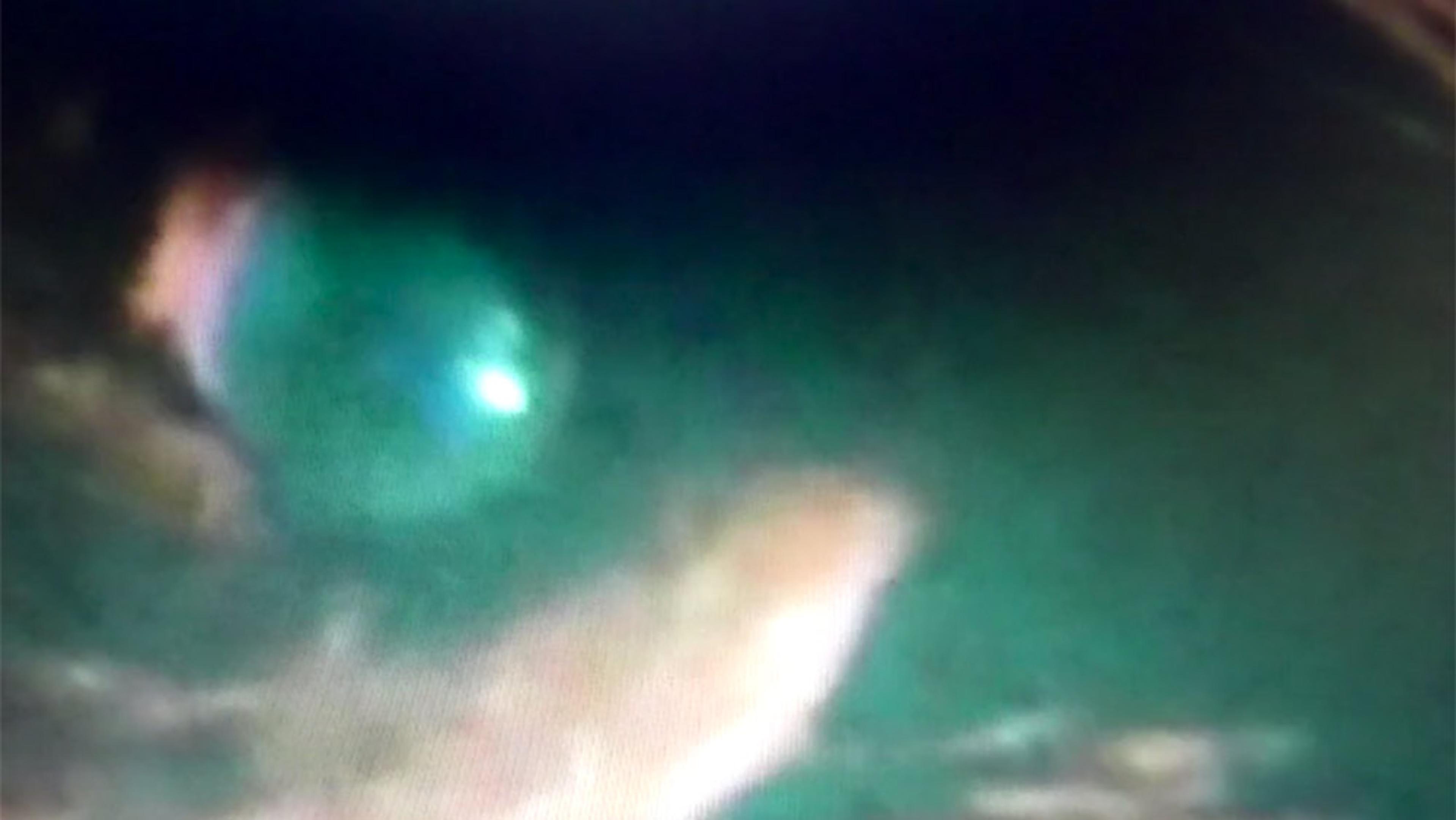 Blurry underwater photo resembling a close-up green eye reflecting light. The image has soft, out-of-focus details.
