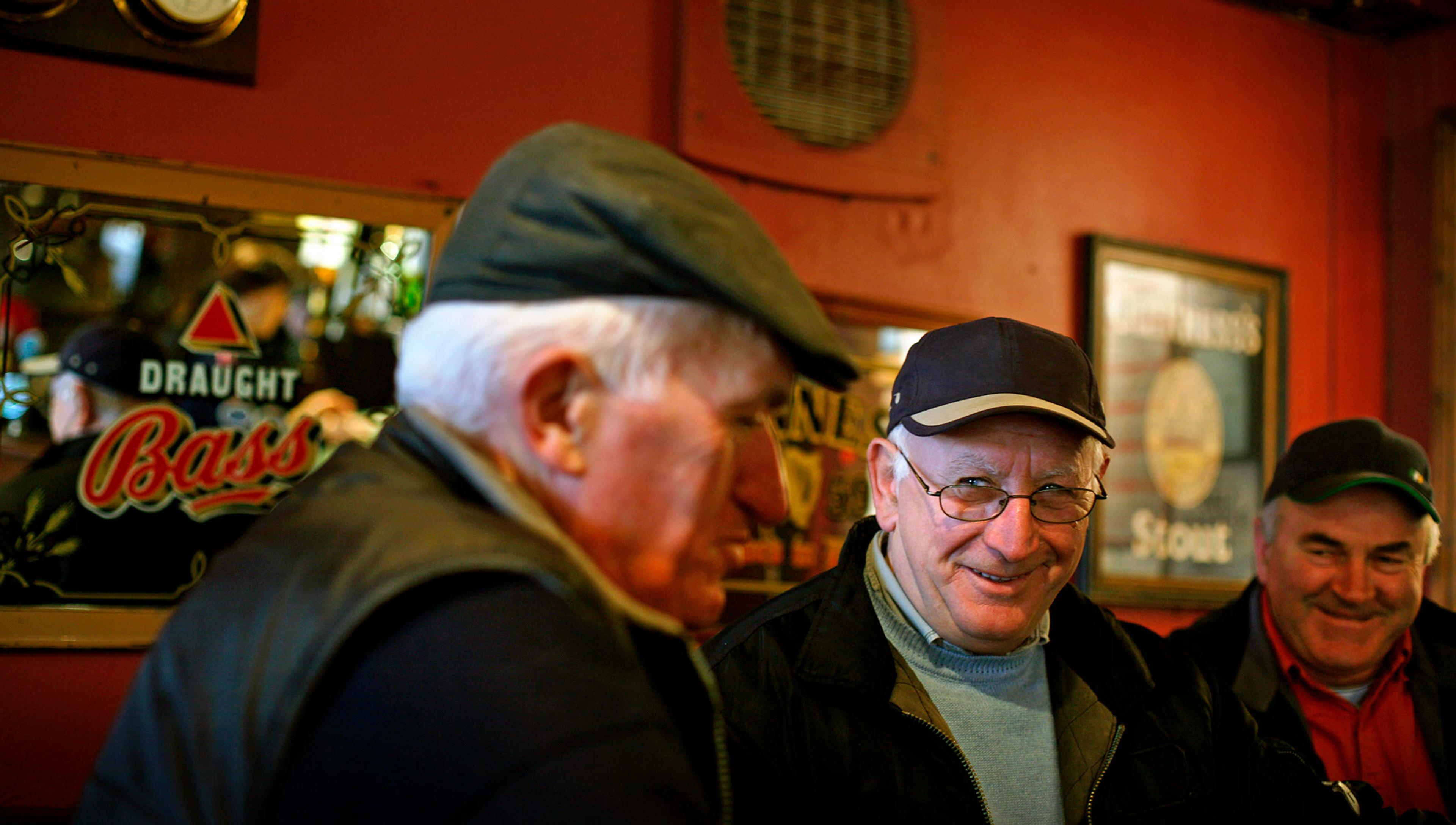 Three older men in cheerful mood are inside a bar or pub with painted red walls