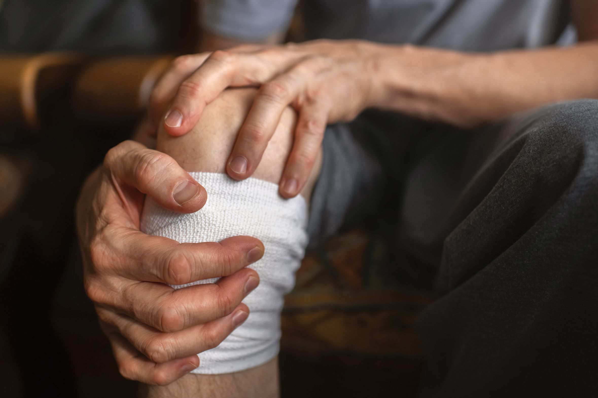 Hands holding an injured leg with a white bandage, suggesting pain or support for the joint.