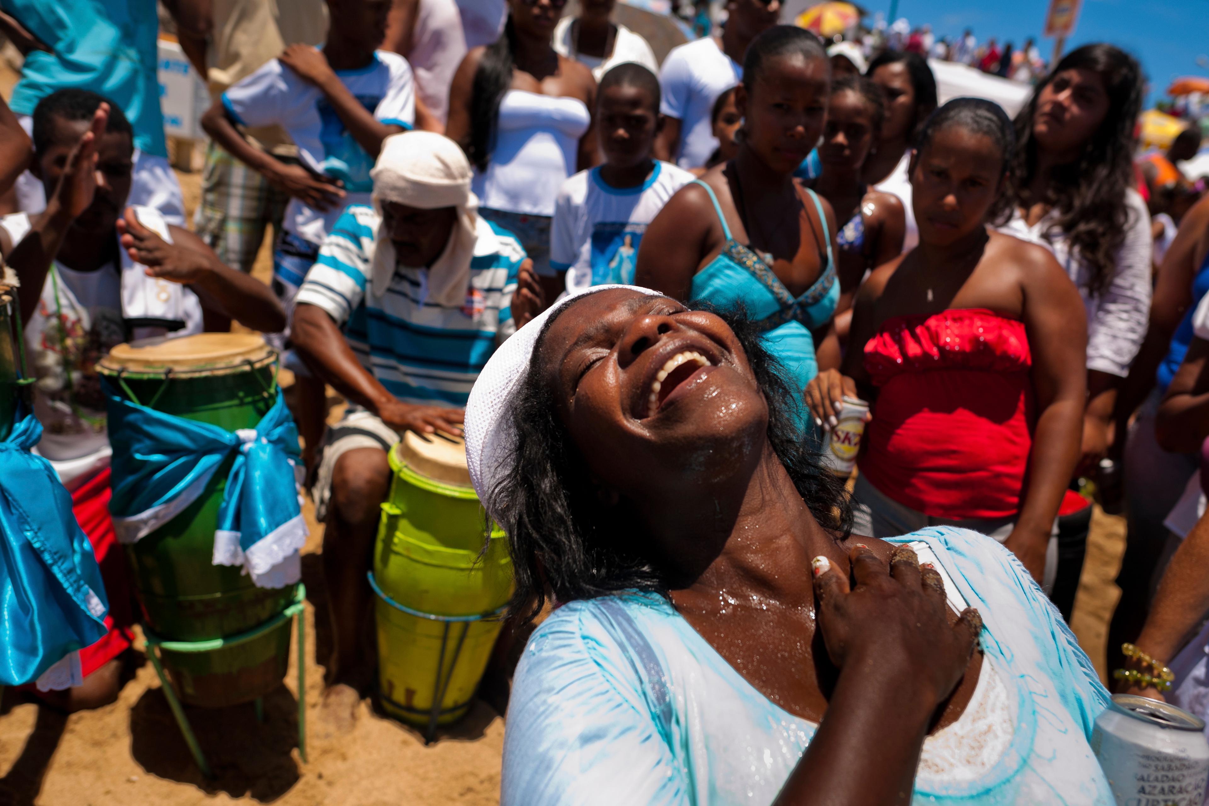 Photo of a joyful woman at a beach festival surrounded by people and drummers, reflecting vibrant energy and celebration.