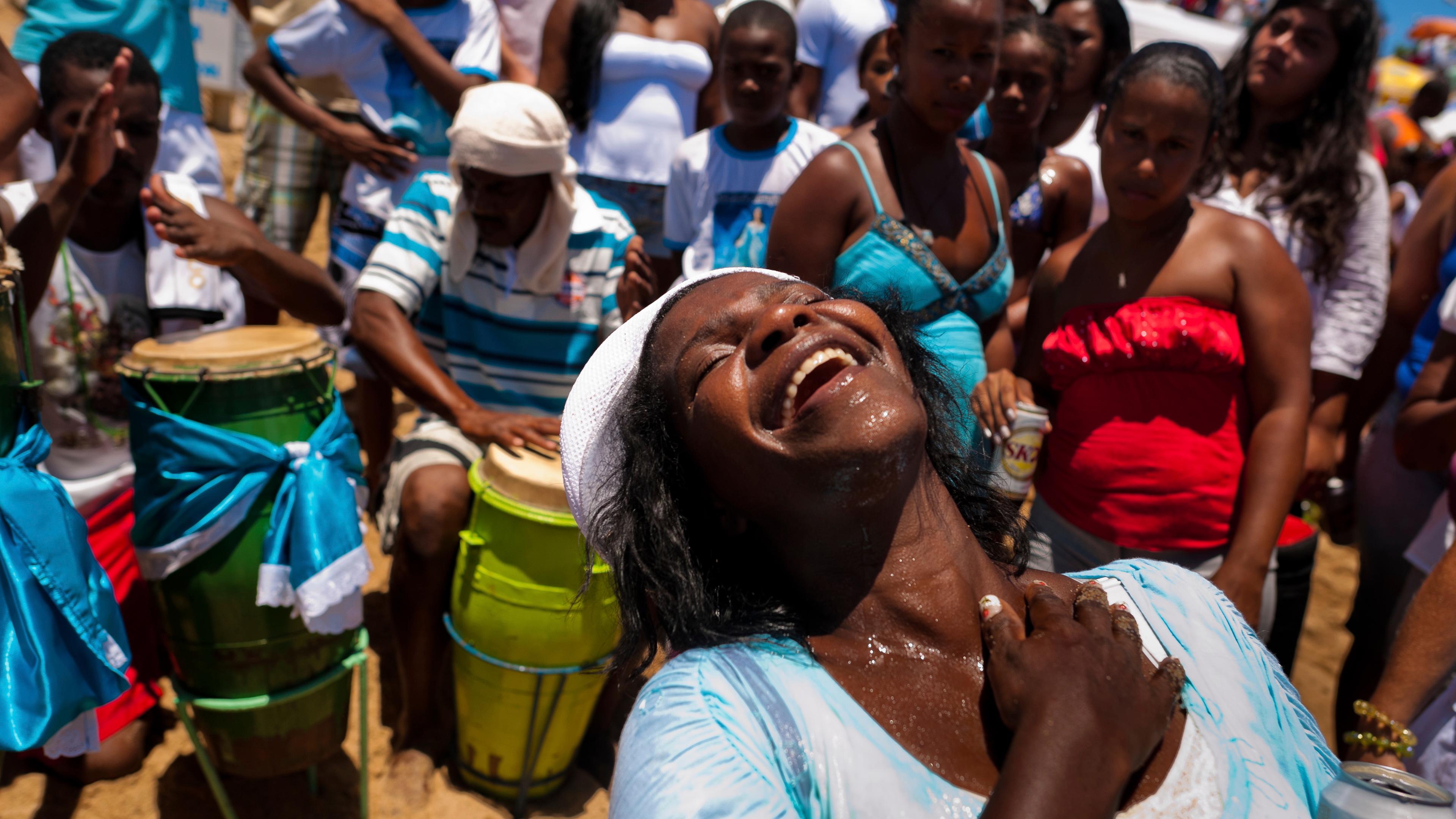 Photo of a joyful woman at a beach festival surrounded by people and drummers, reflecting vibrant energy and celebration.