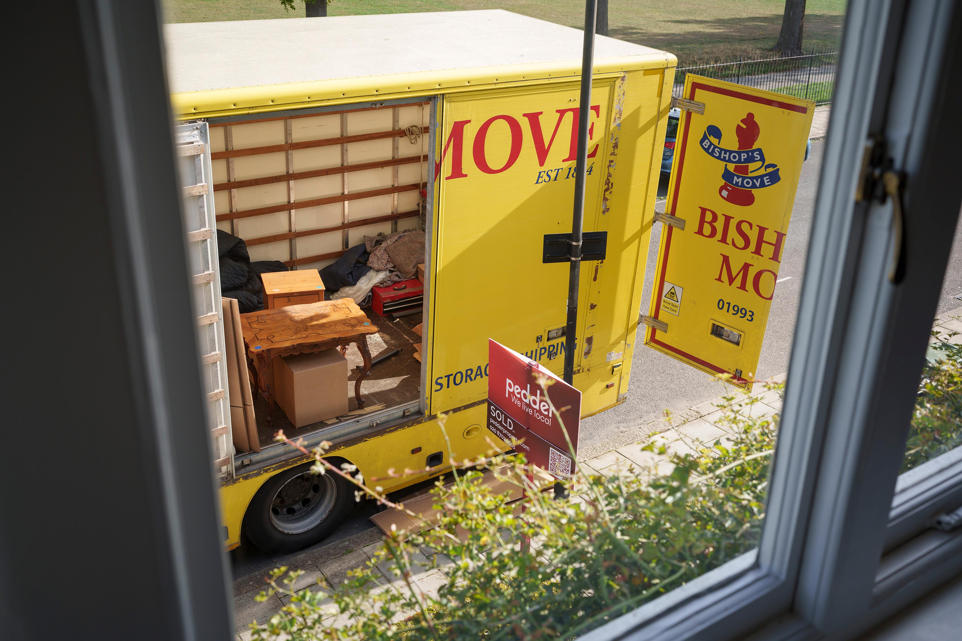A yellow removal van viewed from a window, partially open with furniture and boxes inside on a residential street.
