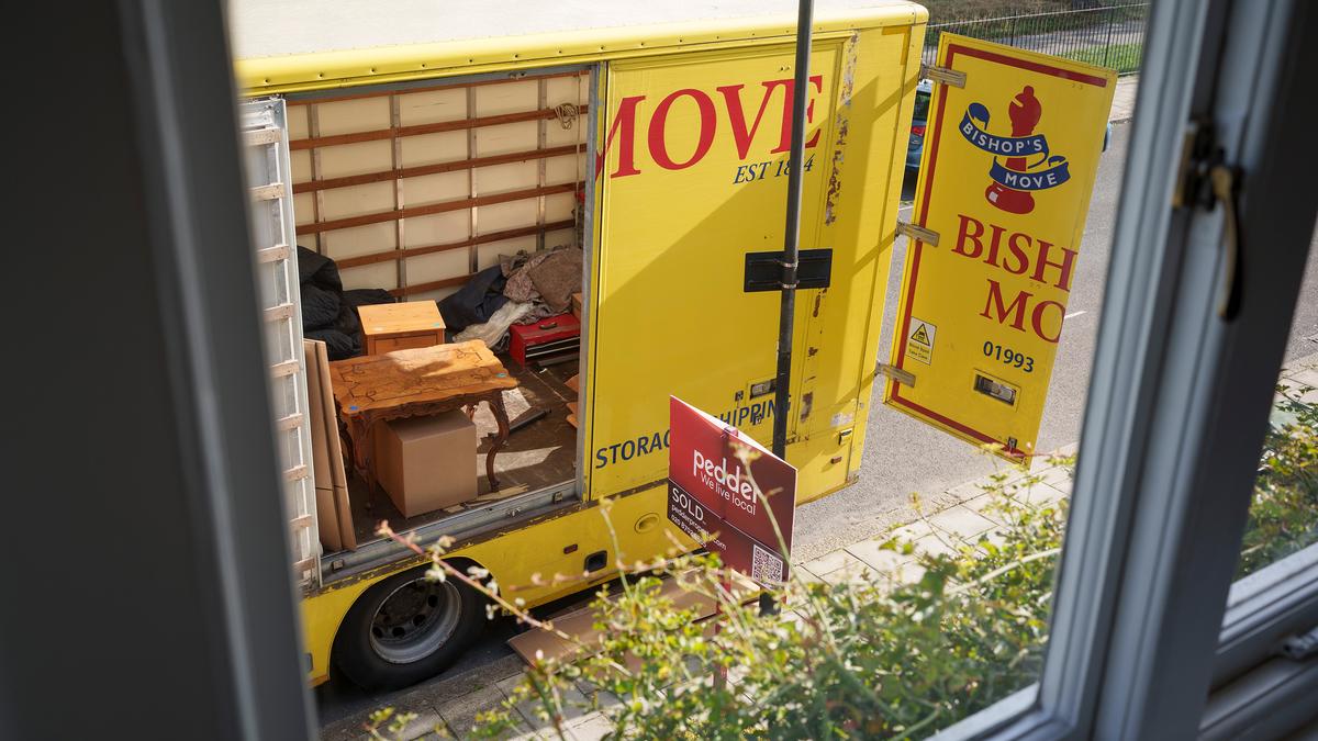 A yellow removal van viewed from a window, partially open with furniture and boxes inside on a residential street.