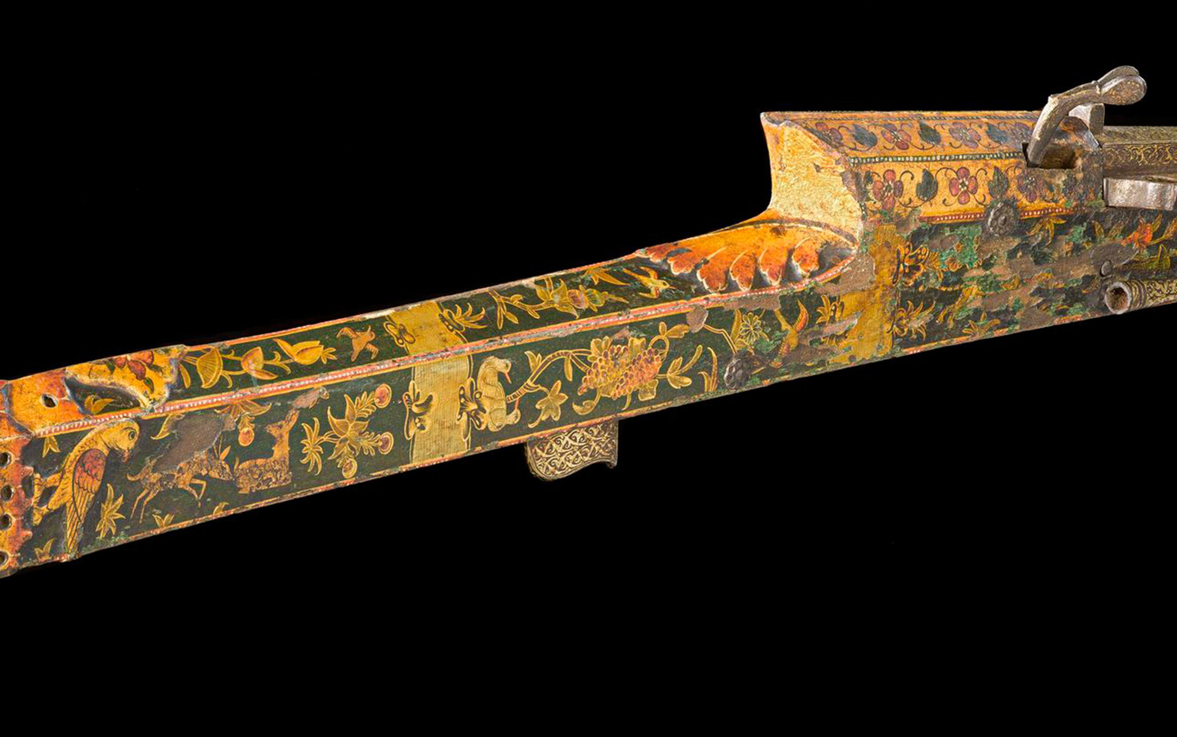 Close-up of an ornately decorated rifle with floral and animal designs on a dark background.