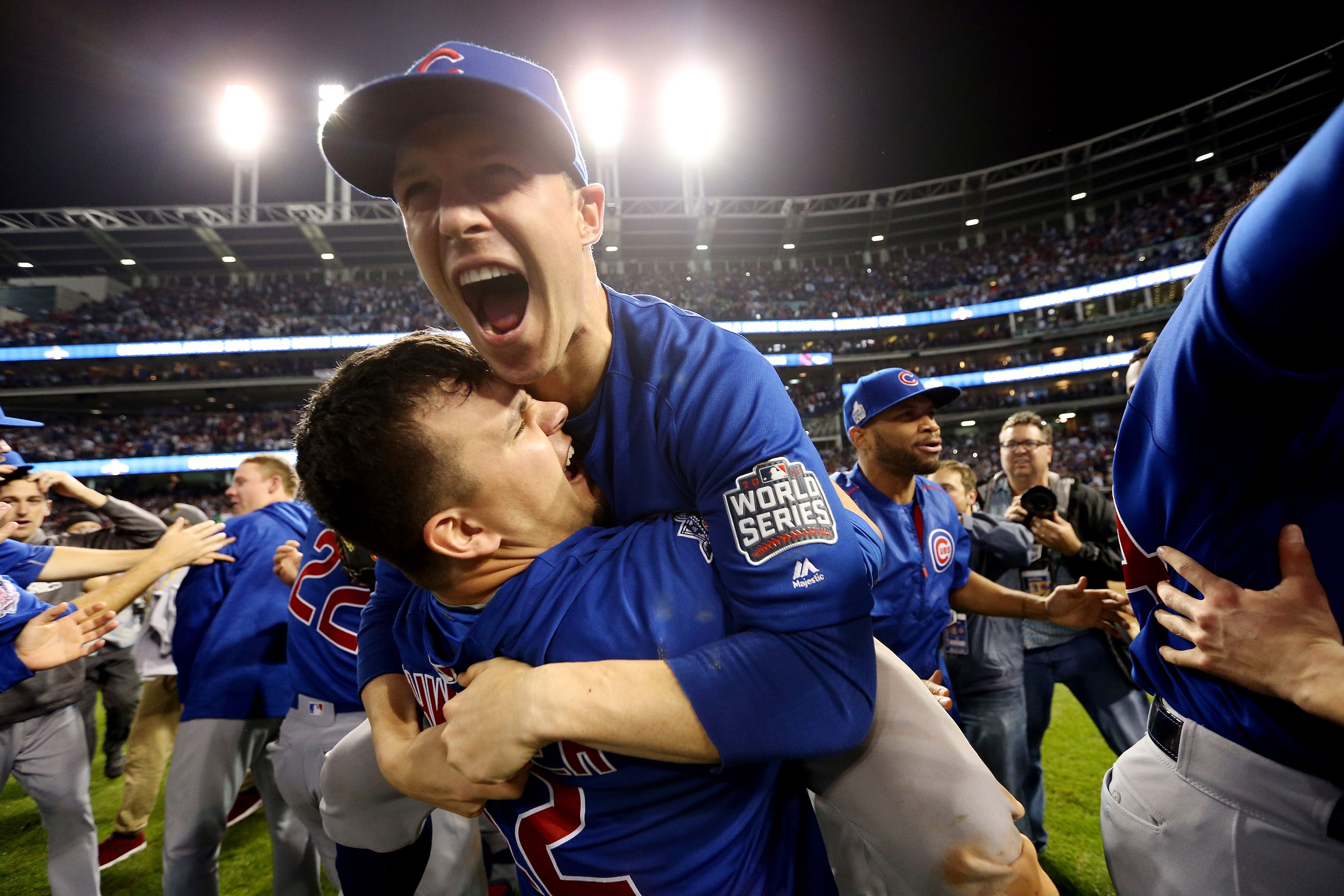 Photo of baseball team celebrating on-field victory under bright lights, players wearing blue jerseys with World Series patch.