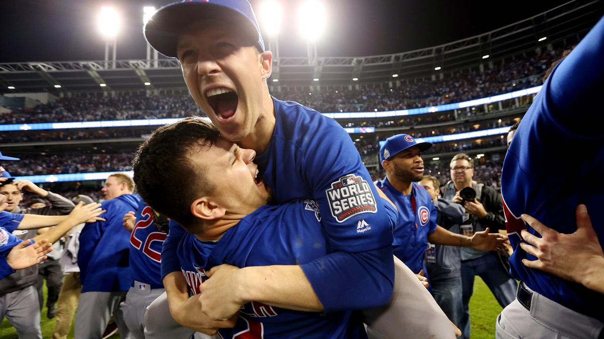 Photo of baseball team celebrating on-field victory under bright lights, players wearing blue jerseys with World Series patch.