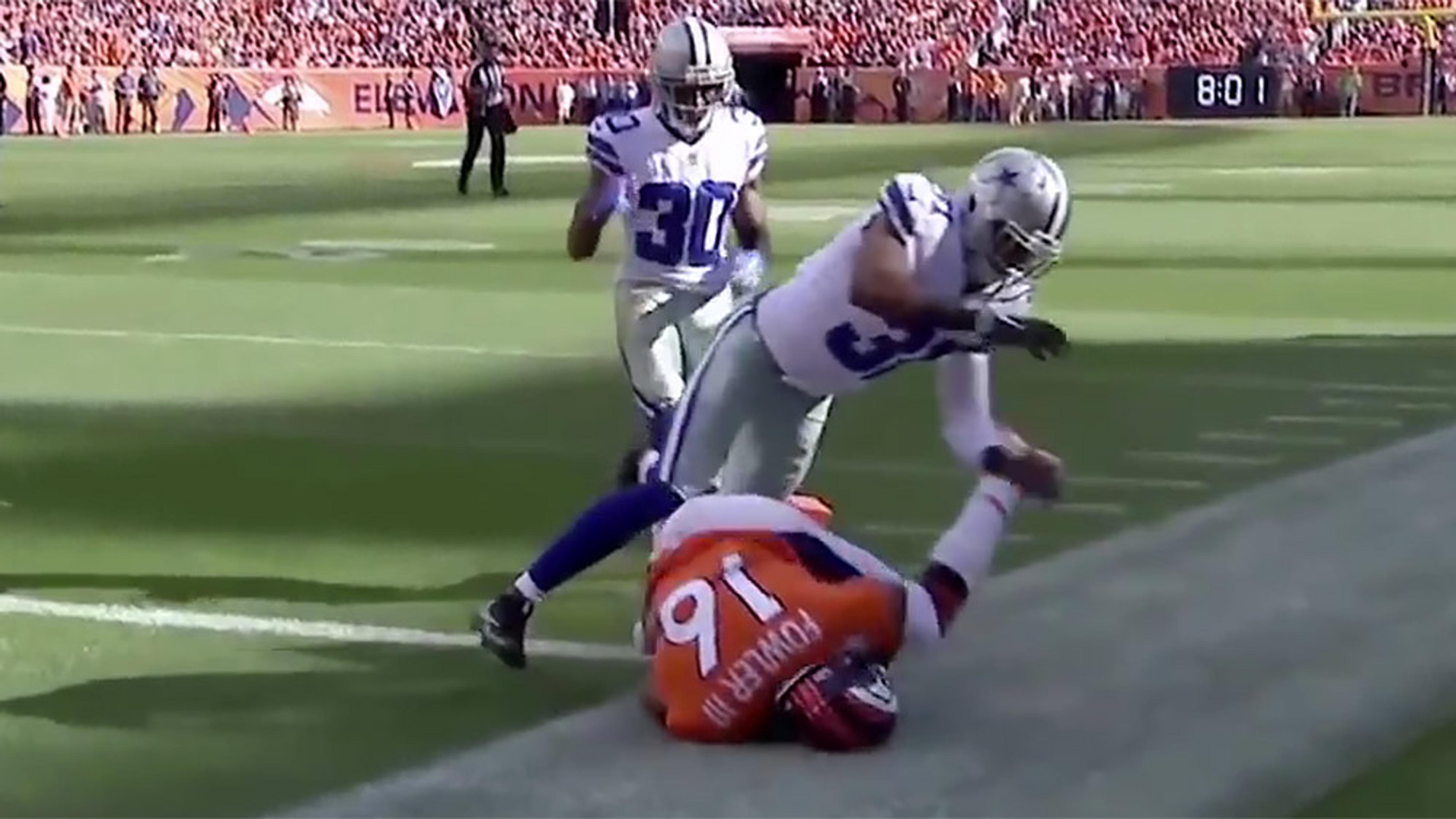 Two American football players in white uniforms tackling a player in an orange uniform at the edge of the field.