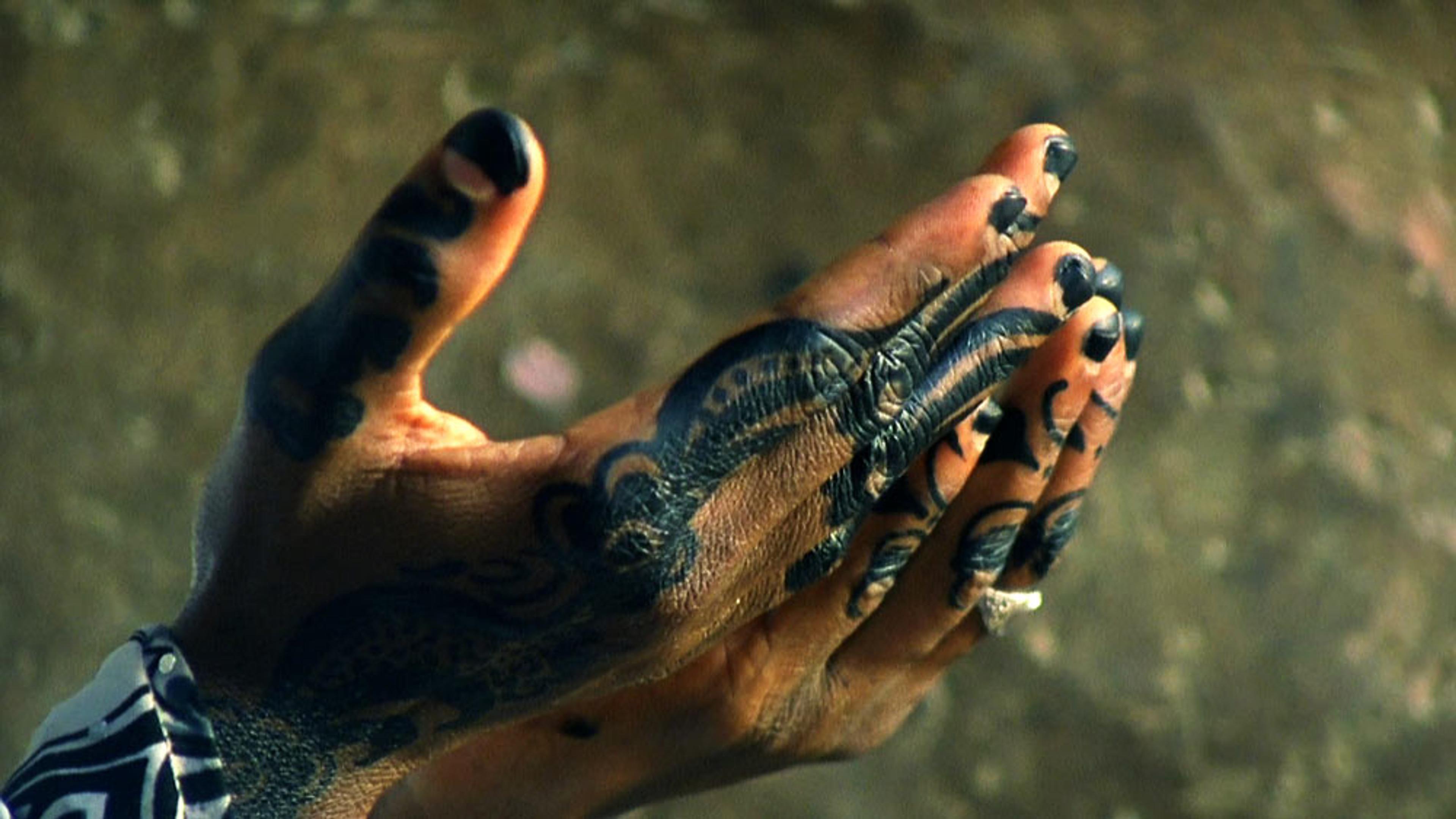 Hands with intricate black tattoos held together against a blurry background.