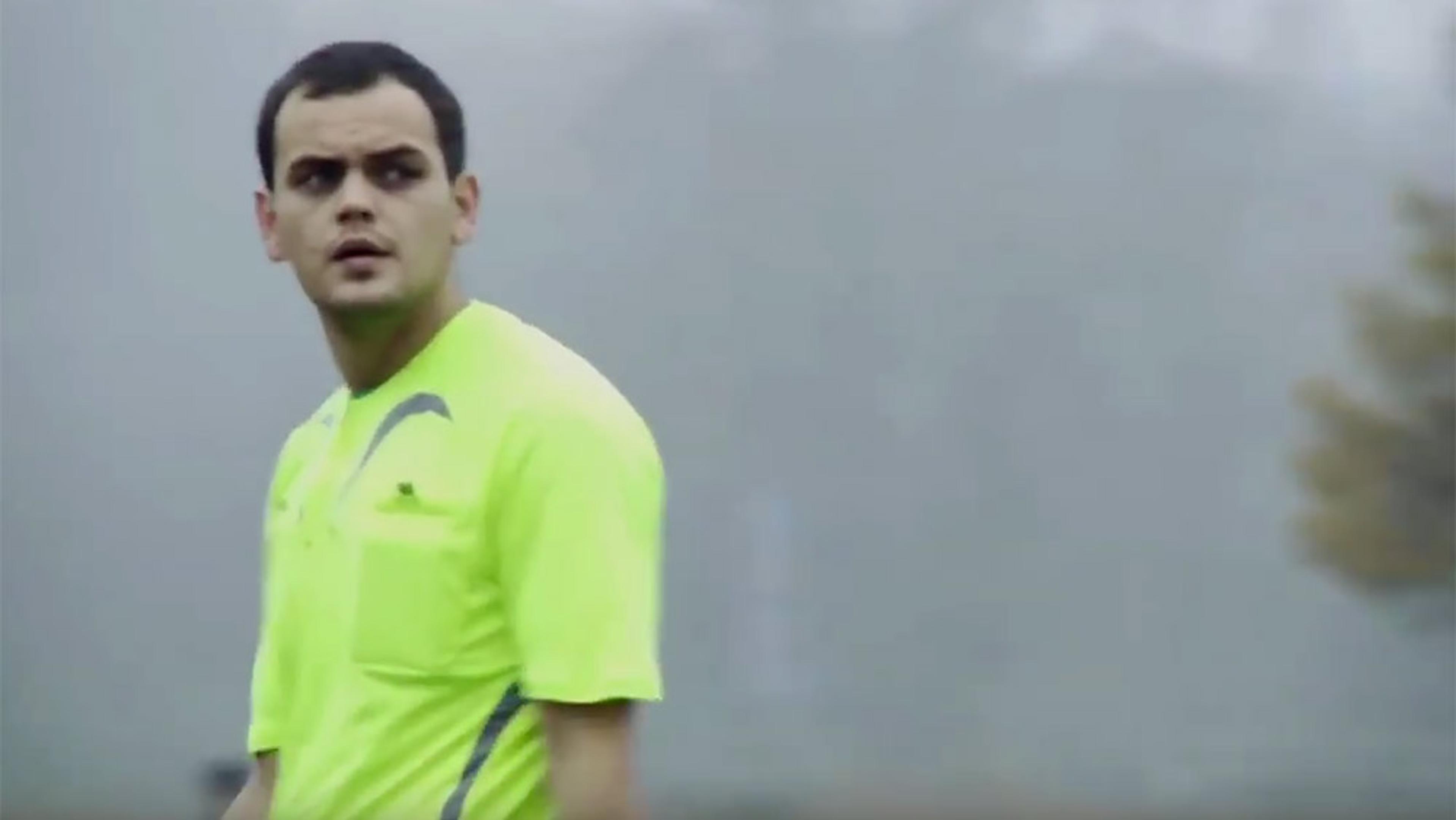 A man wearing a neon yellow sports shirt standing outdoors on a foggy day, looking to his left.