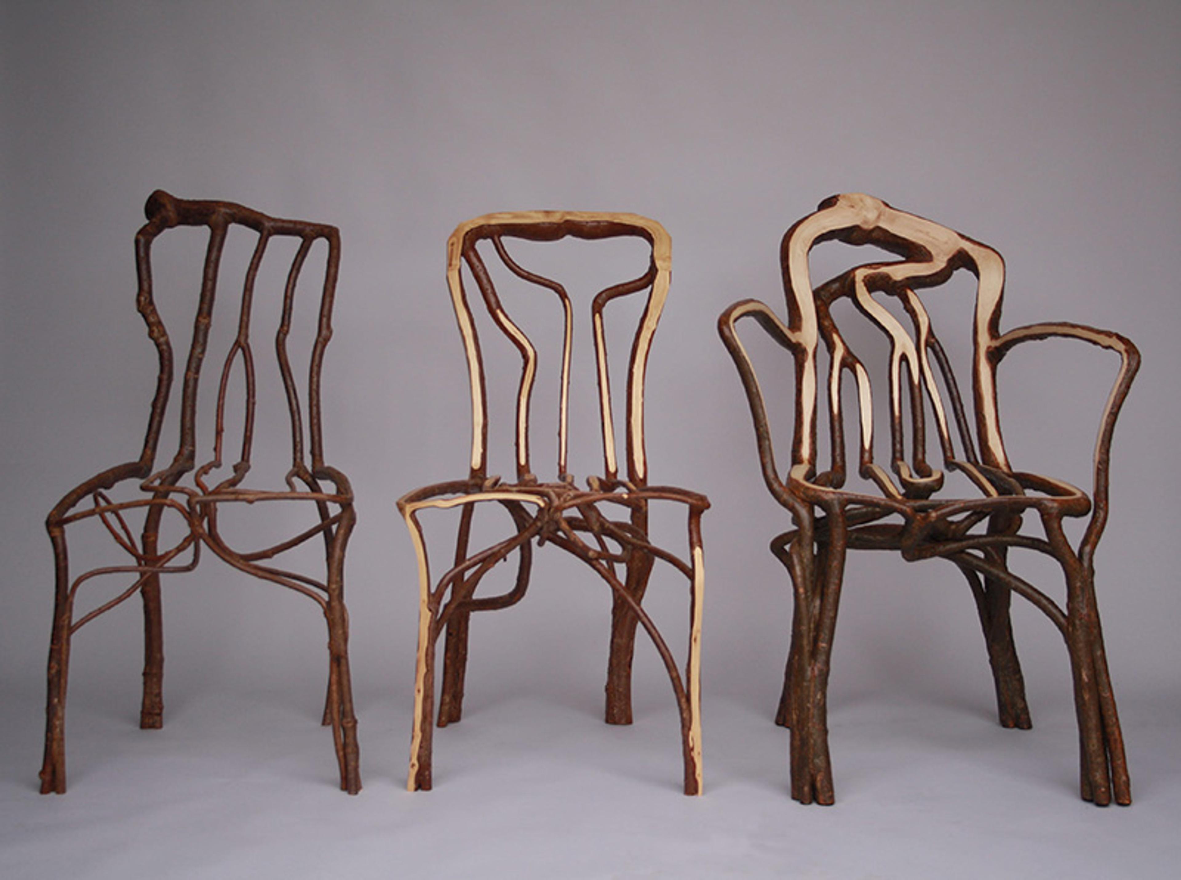 Three wooden chairs made from intertwining tree branches against a plain grey background.