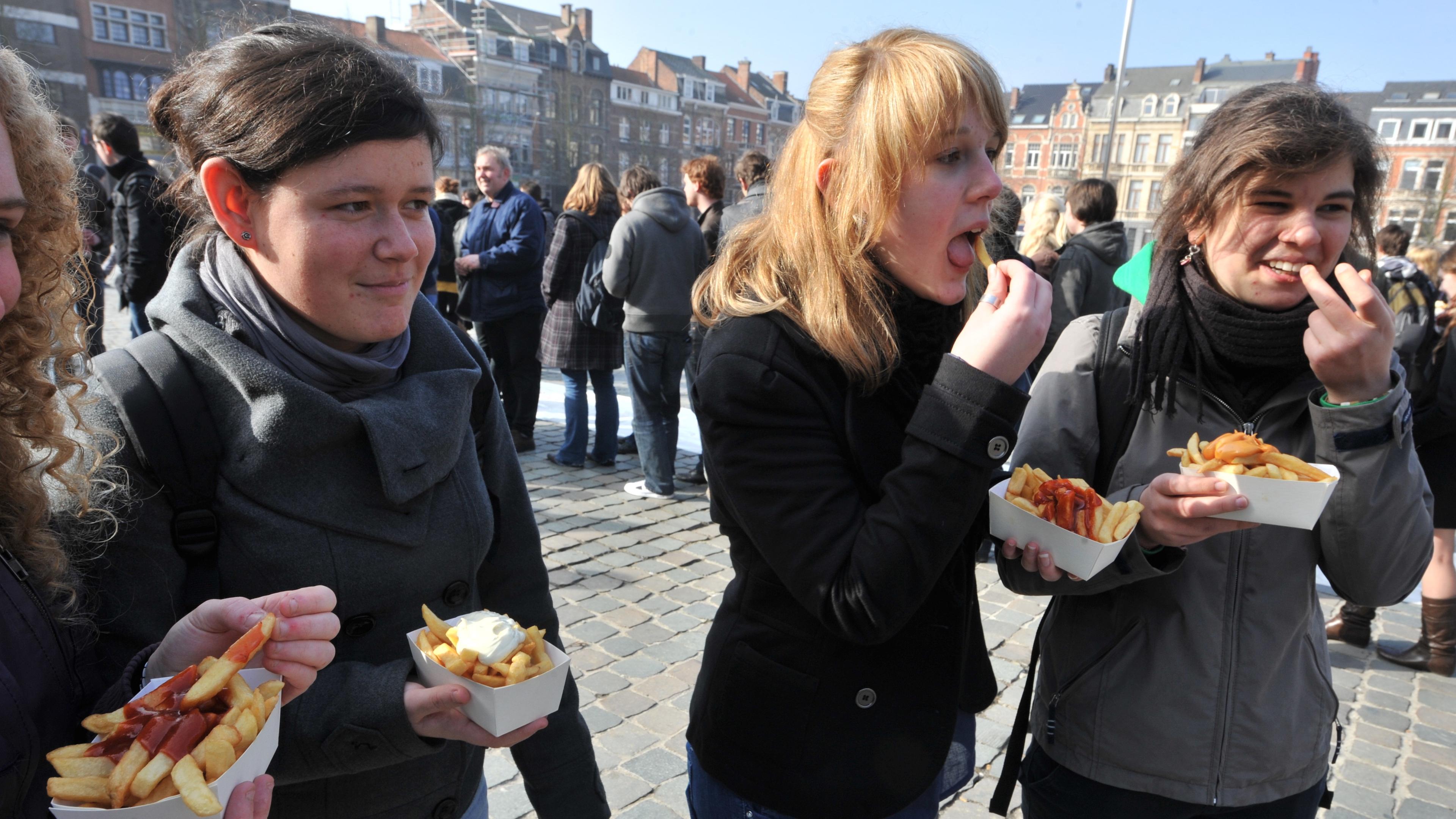 Photo of four people outdoors eating chips with sauce from trays on a cobblestone street with buildings in the background.