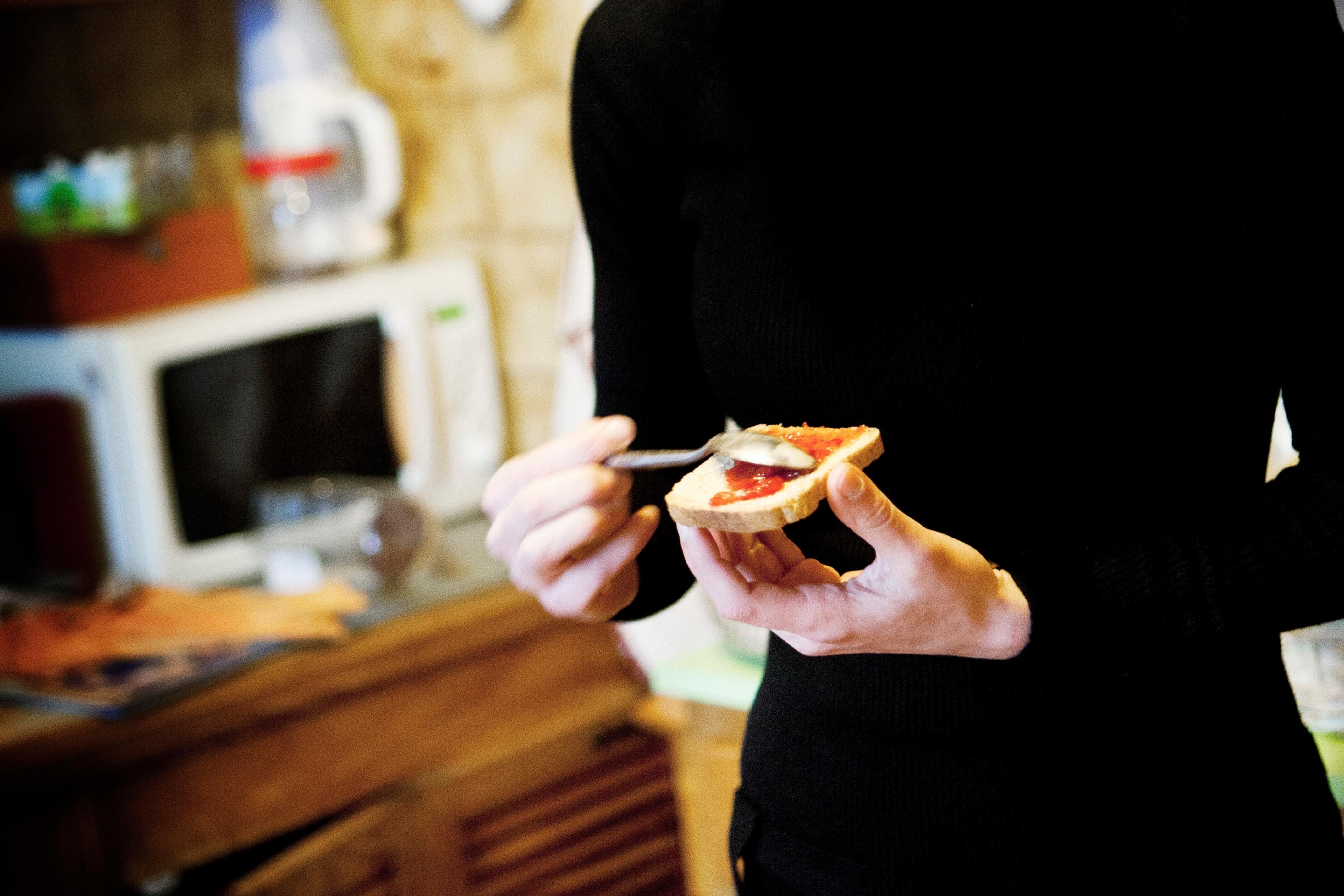Photo of a woman in a kitchen spreading jam on toast with a spoon.