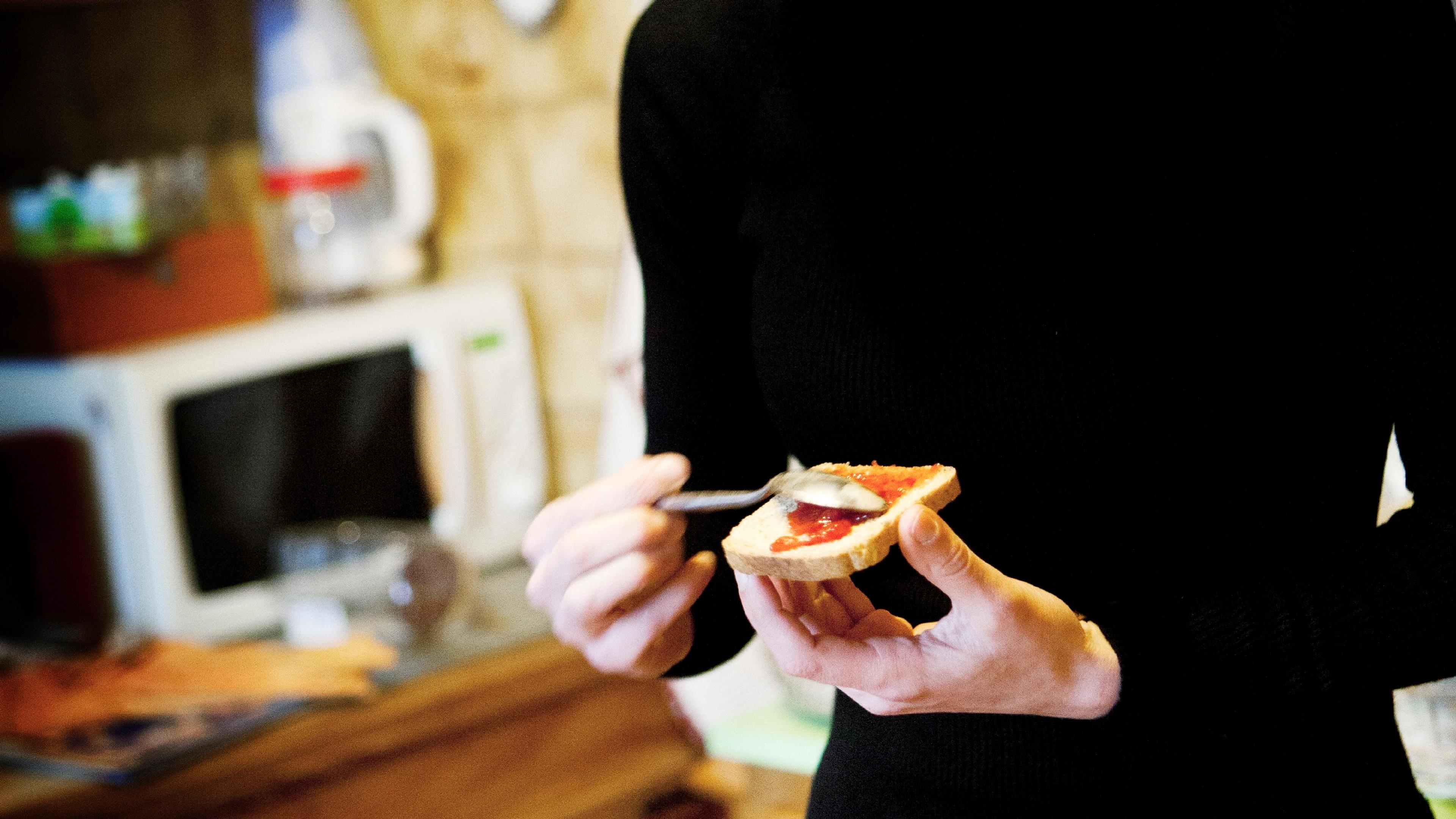 Photo of a woman in a kitchen spreading jam on toast with a spoon.