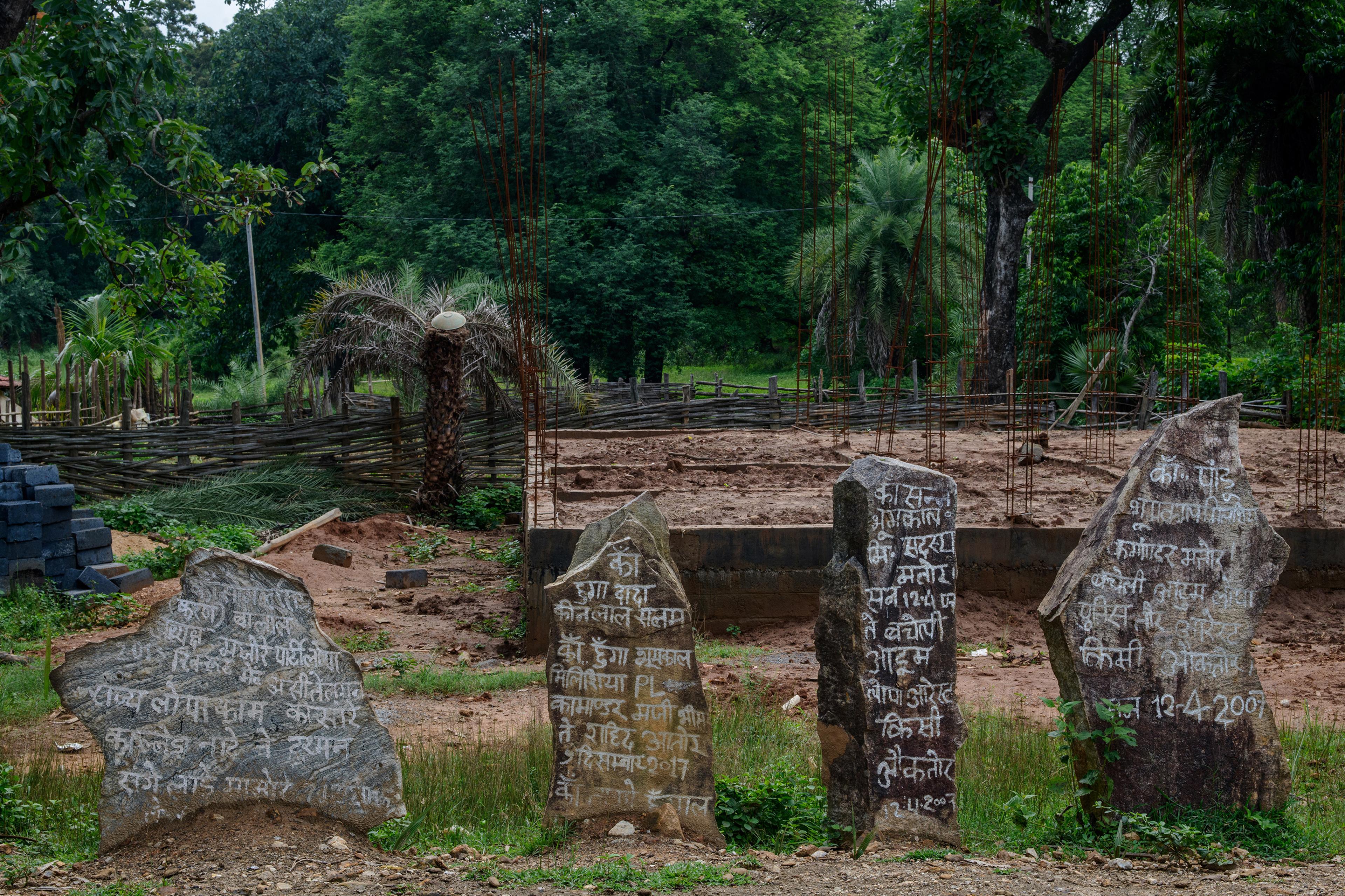 Photo of a construction site with wooden fence, trees and stones inscribed with Hindi text in the foreground.