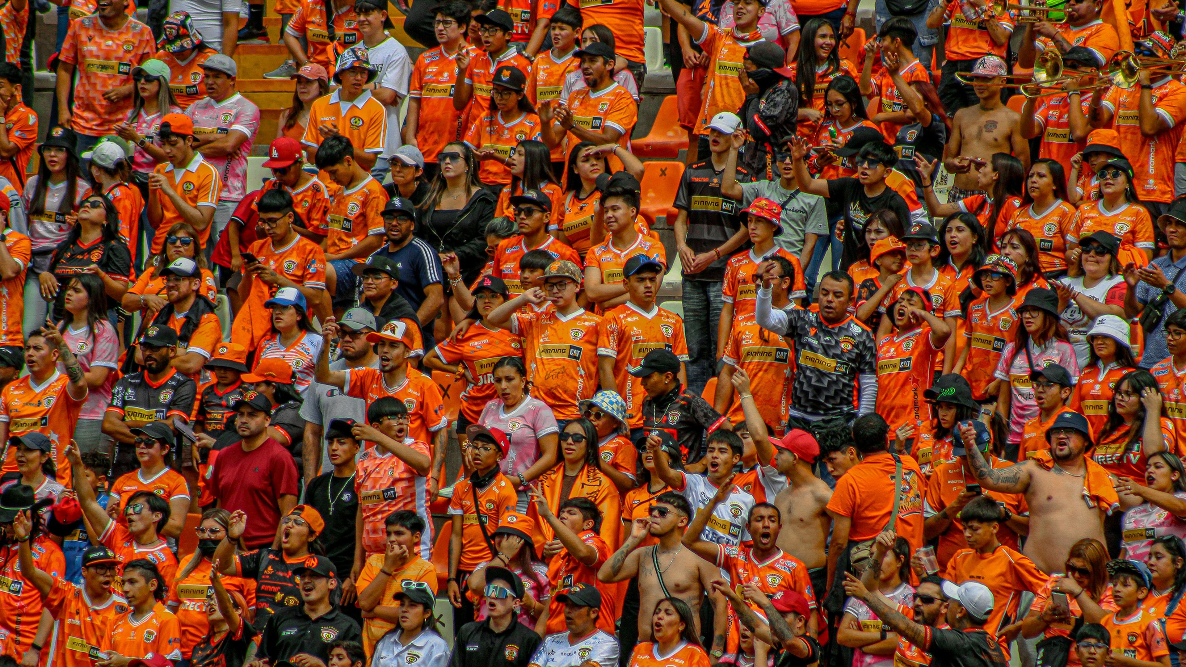 Una multitud entusiasmada con camisetas naranjas anima en un evento deportivo, mostrando la diversidad de los aficionados en el ambiente de un estadio.