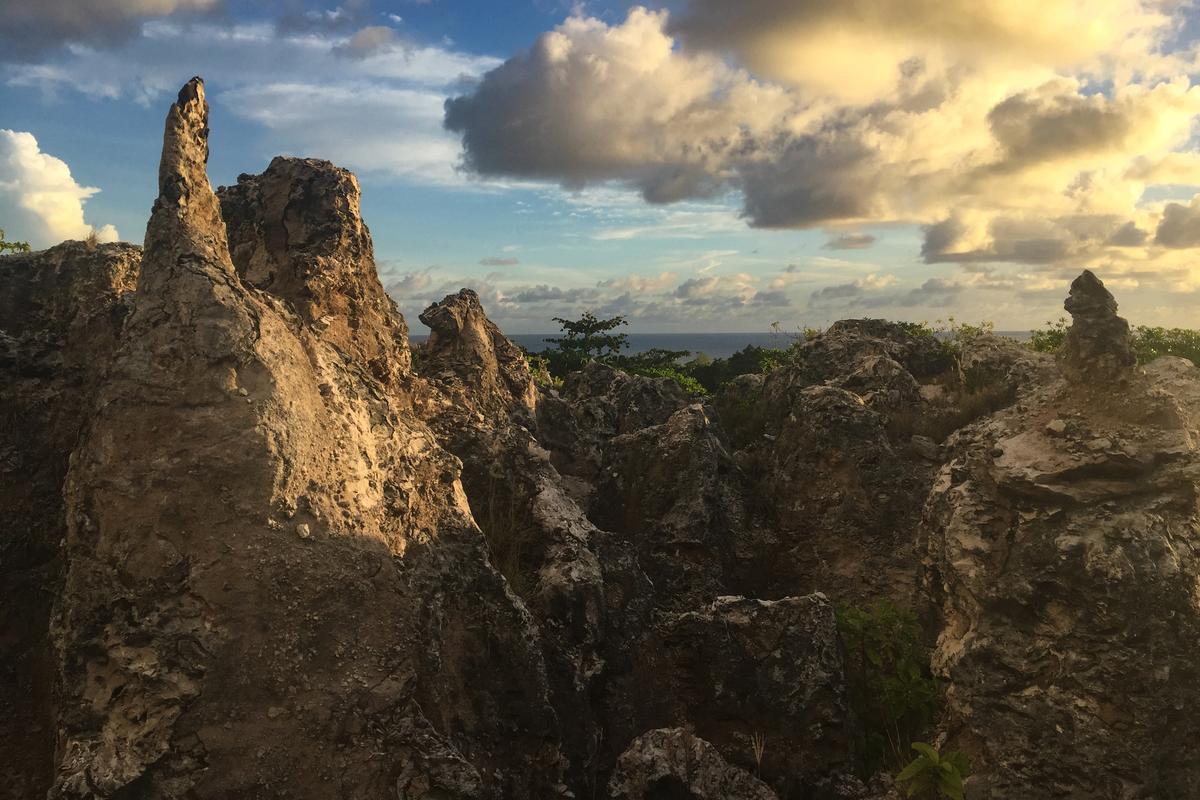 Photo of rugged limestone formations at sunset with a partly cloudy sky and sea visible in the background.