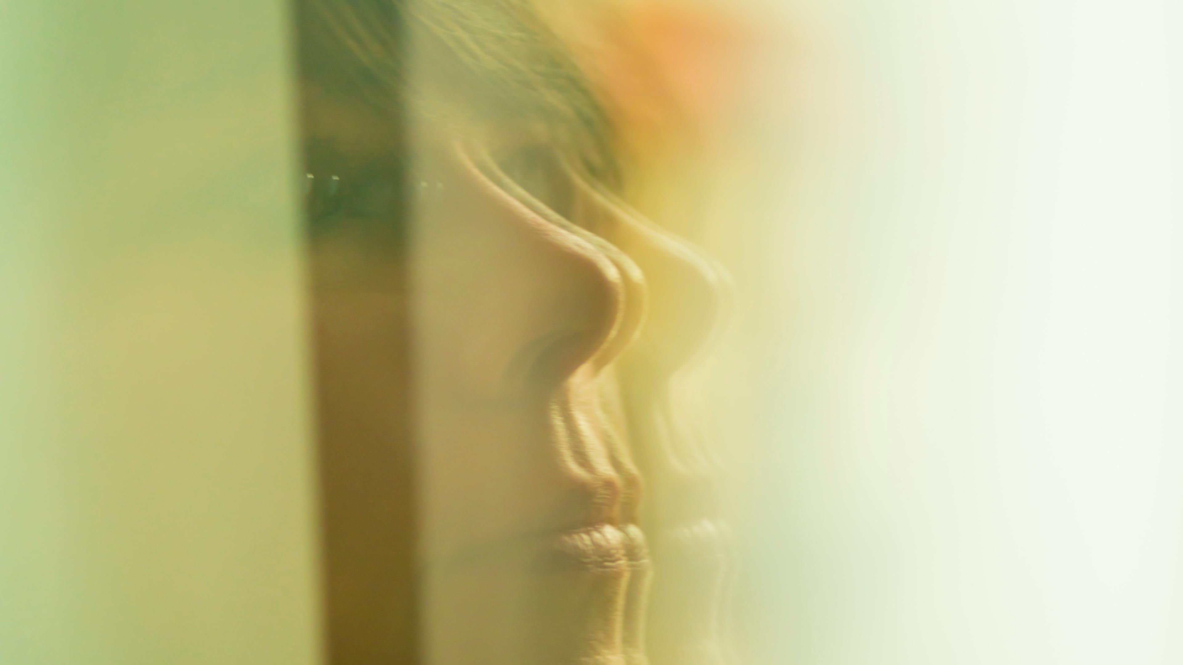 Photo of a woman’s face reflected in a glass window with soft, abstract focus and greenish tones.