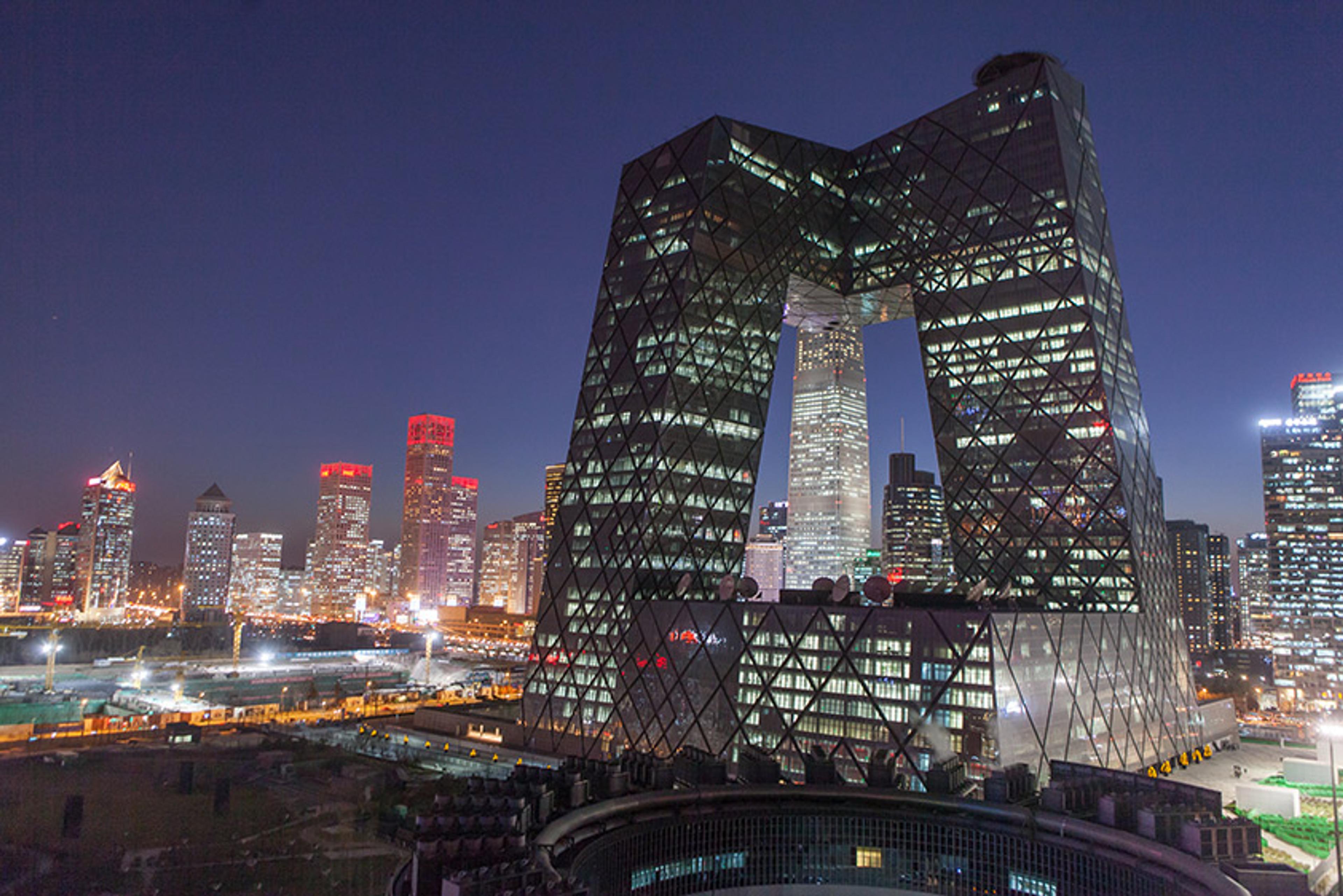 A city skyline at night featuring a unique geometric building with interlocking sections, illuminated with bright lights.