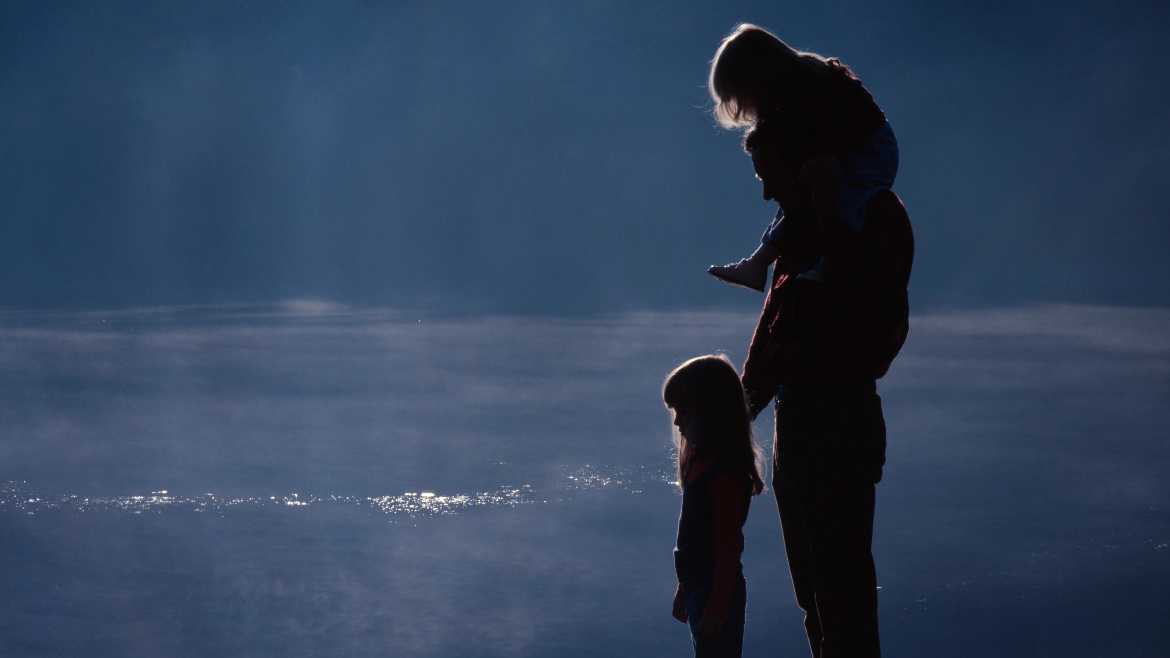 Silhouetted photo of a family on a wooden pier overlooking a serene lake at sunset.