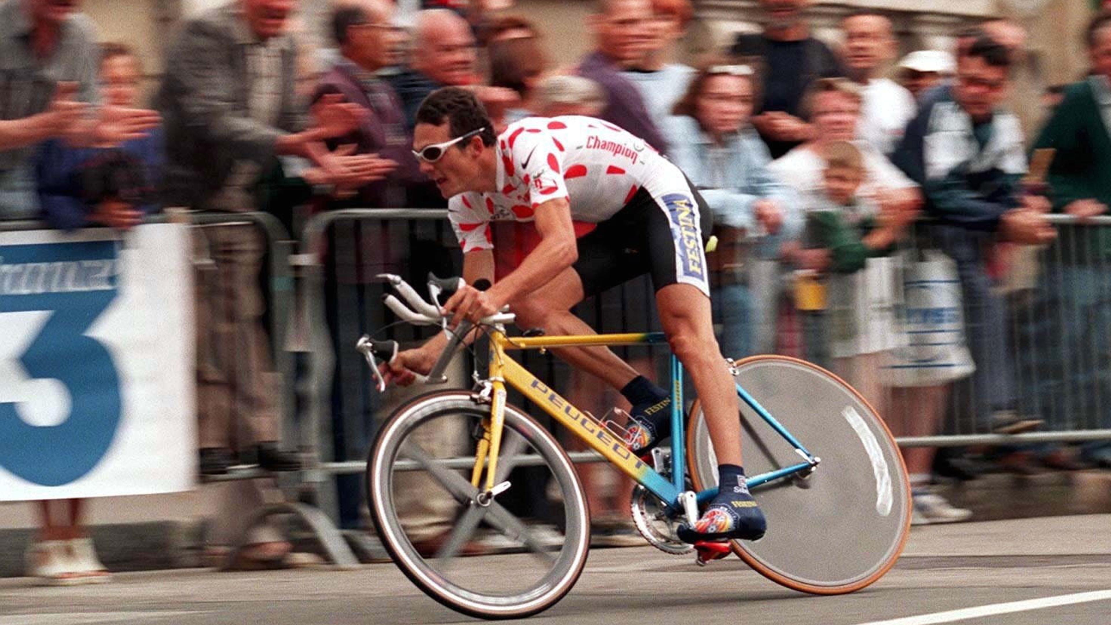 Photo of a cyclist in a red polka dot jersey racing past a cheering crowd on a yellow bicycle.