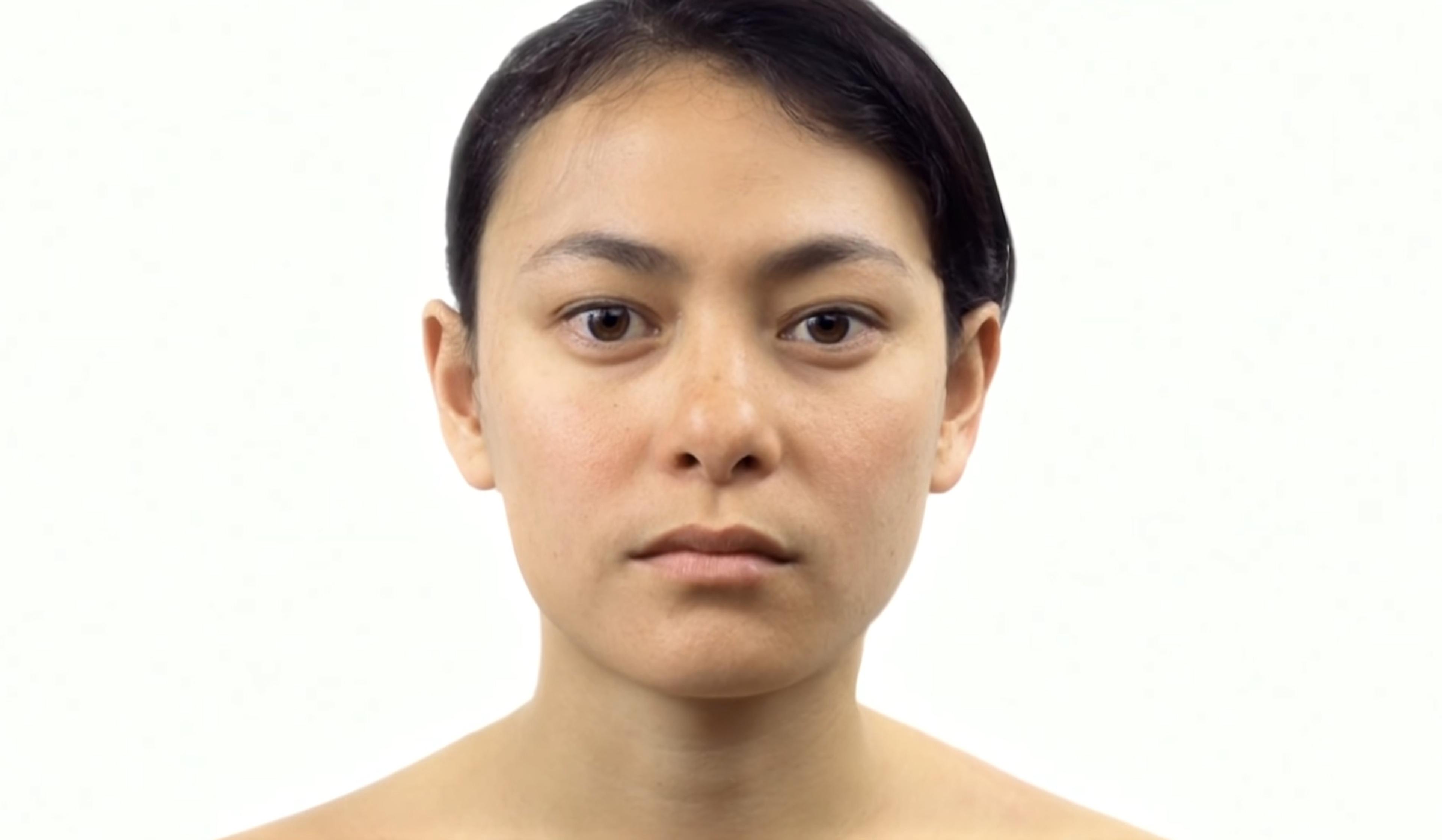 Close-up of a woman with short dark hair, neutral expression, and bare shoulders against a plain white background.