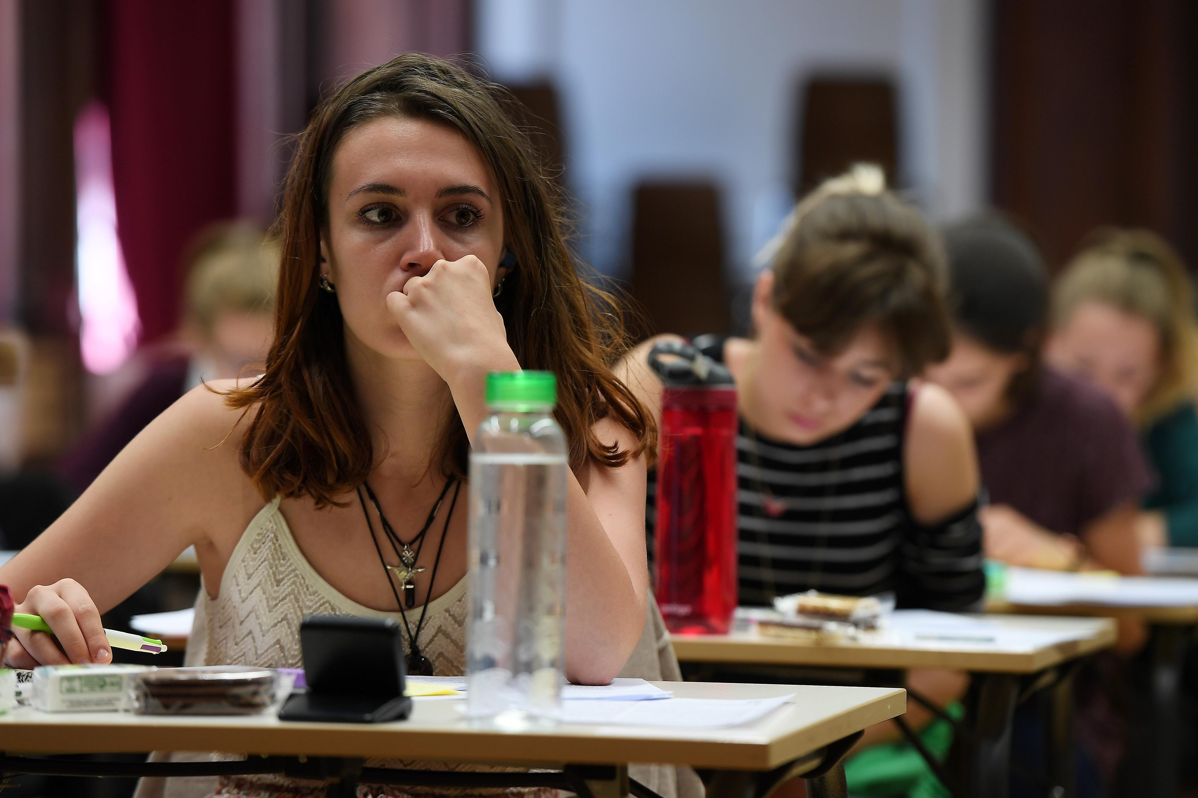 Photo of students sitting at desks in a classroom. Focus is on a woman appearing thoughtful with a water bottle nearby.