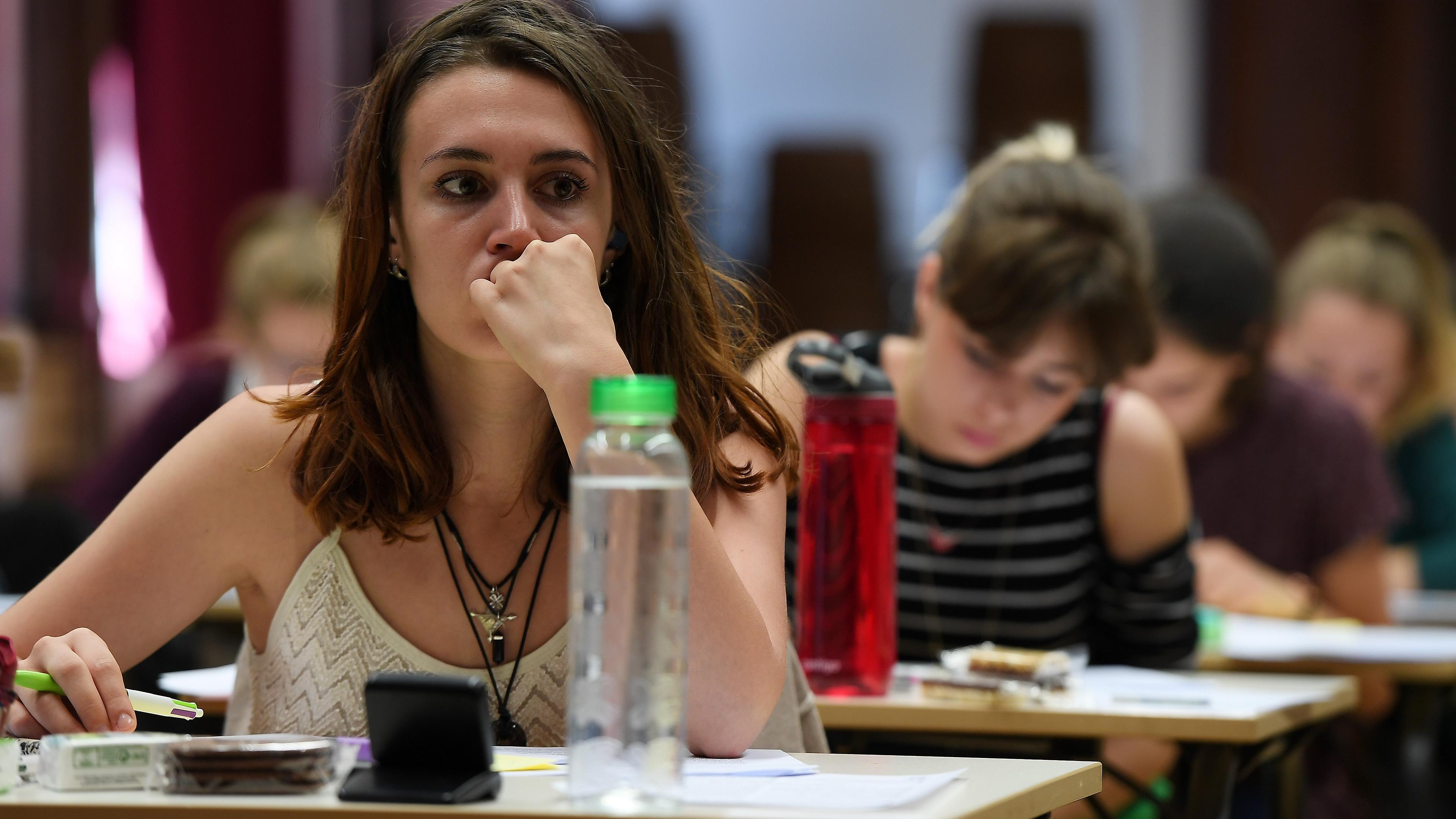 Photo of students sitting at desks in a classroom. Focus is on a woman appearing thoughtful with a water bottle nearby.