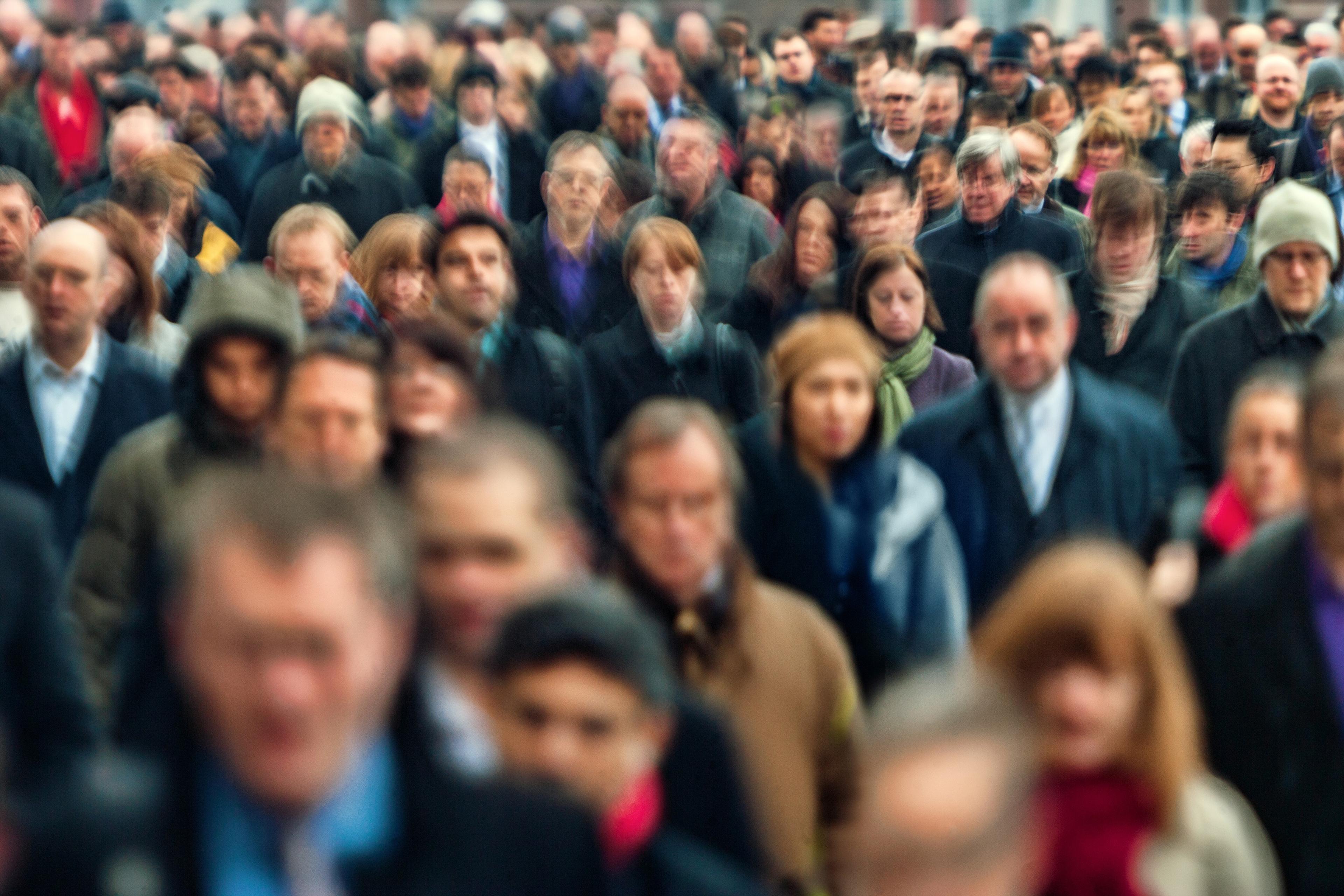 Photo of a large crowd of people walking, with many faces blurred, suggesting movement in an urban setting.