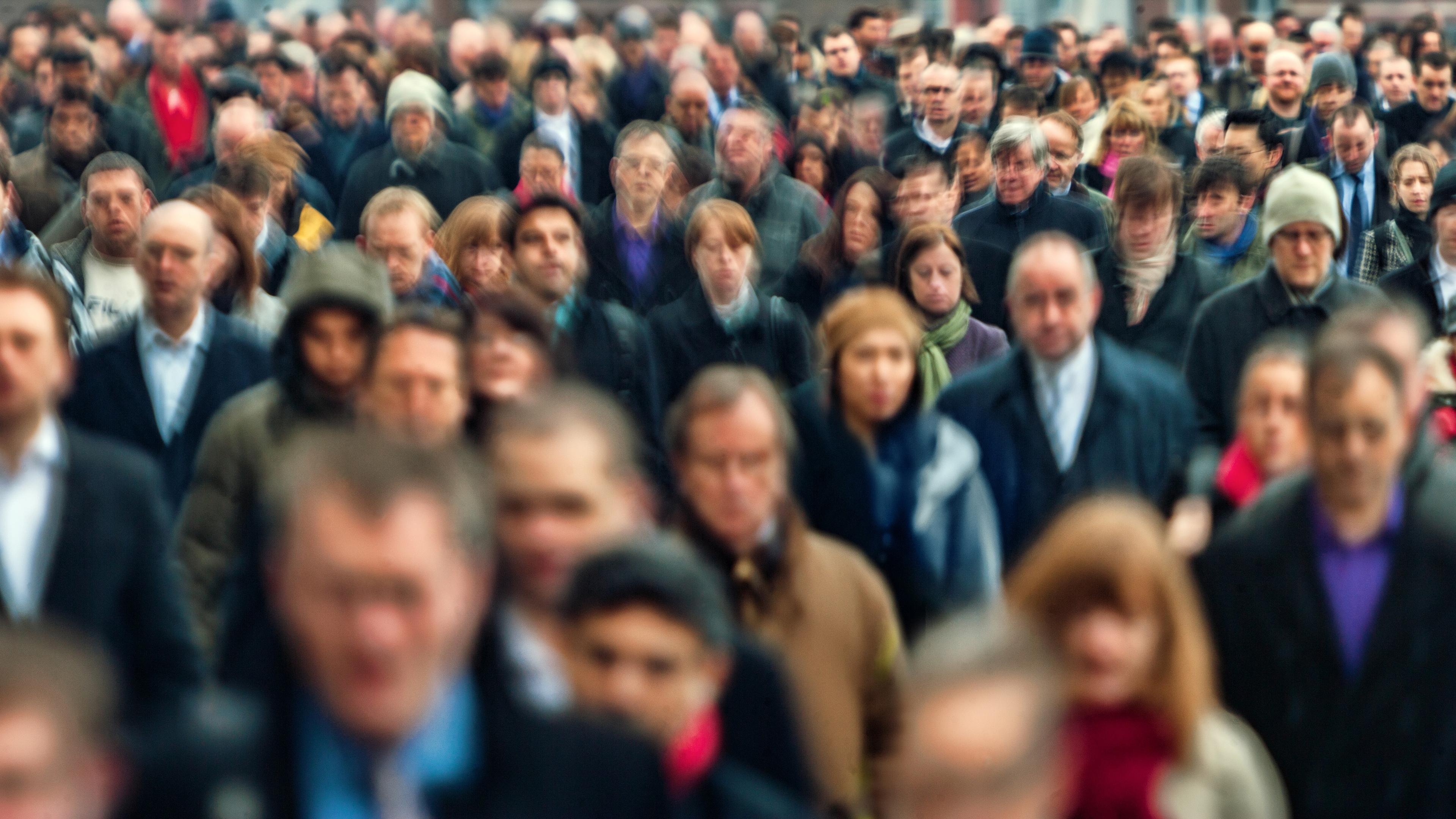 Photo of a large crowd of people walking, with many faces blurred, suggesting movement in an urban setting.