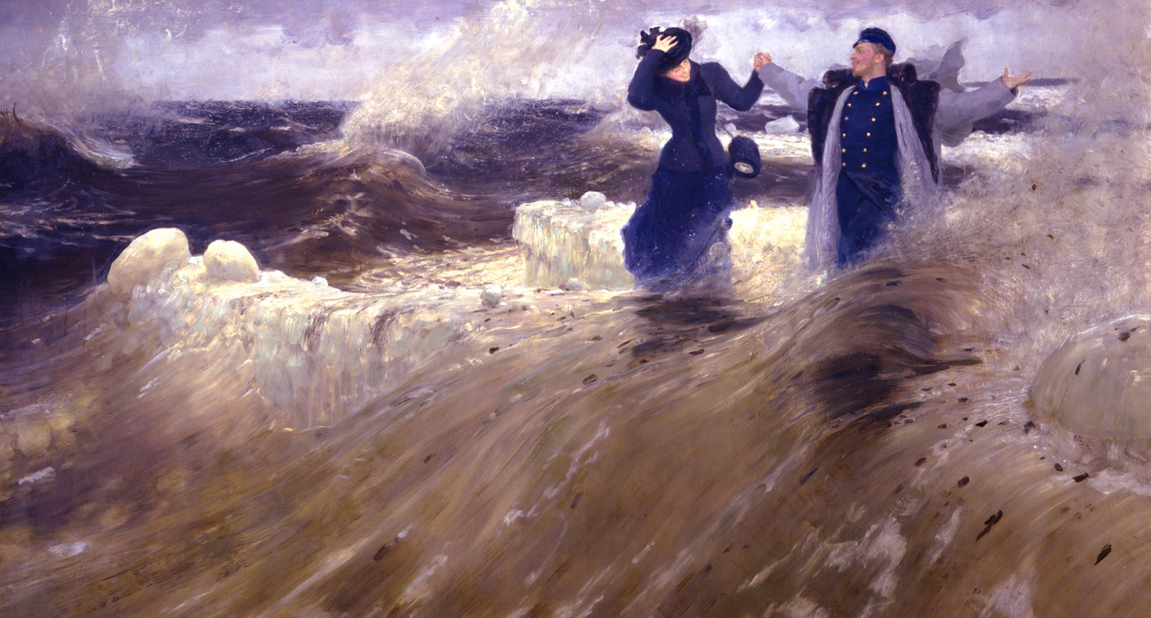 A couple dressed in dark clothes, smiling and holding hands as they walk through stormy seas with crashing waves and a cloudy sky.