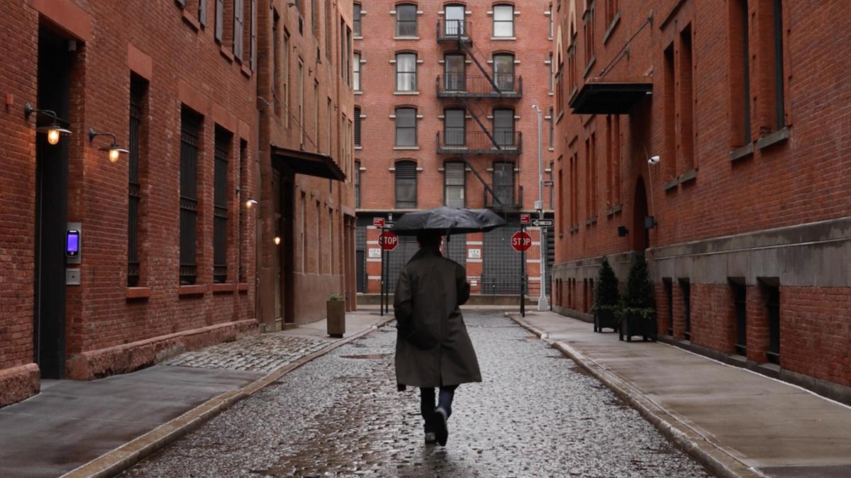 A person with an umbrella walking down a wet brick alley between buildings, with stop signs in the distance.