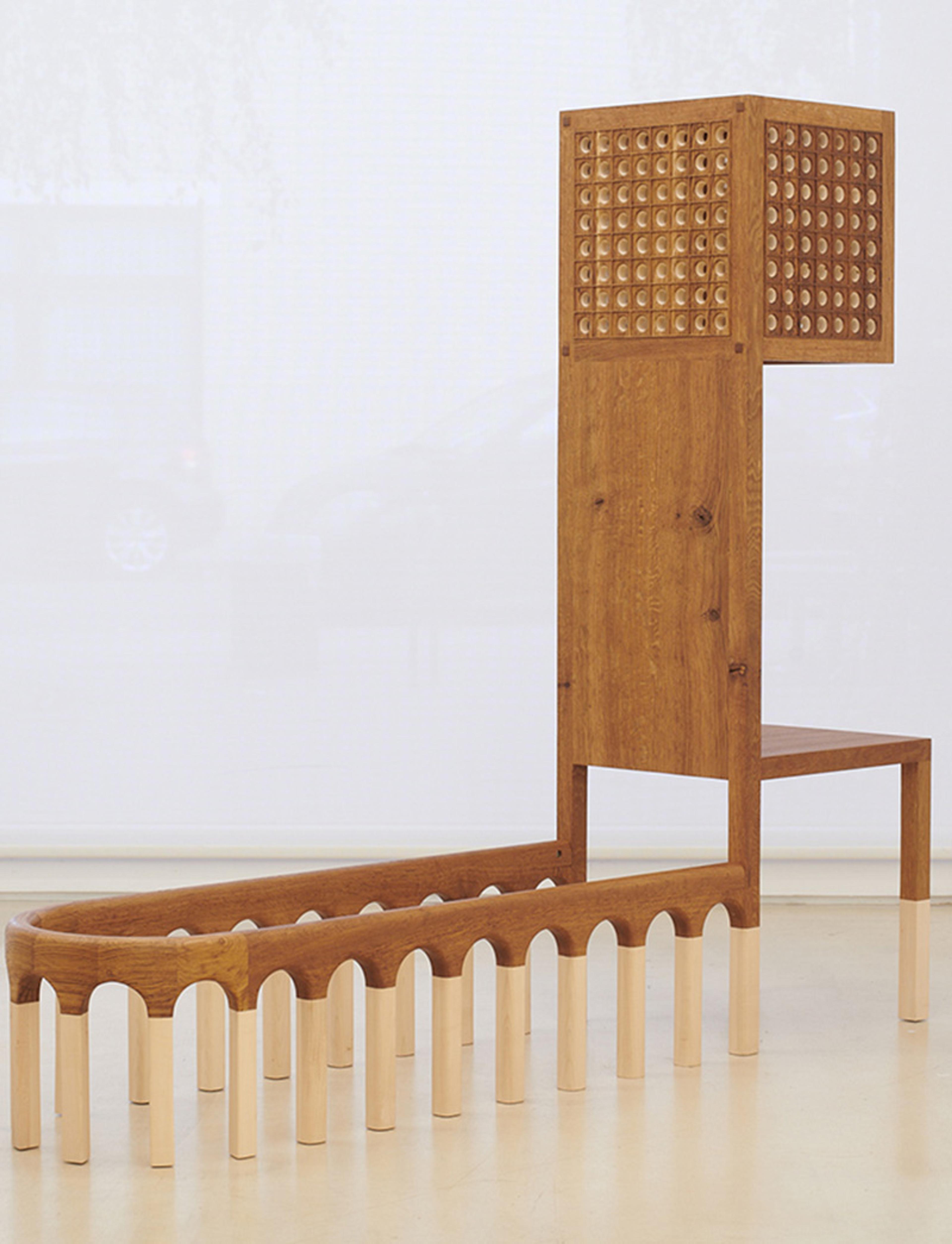 Abstract wooden sculpture featuring a tall boxy structure with a perforated pattern and an elongated arched base.